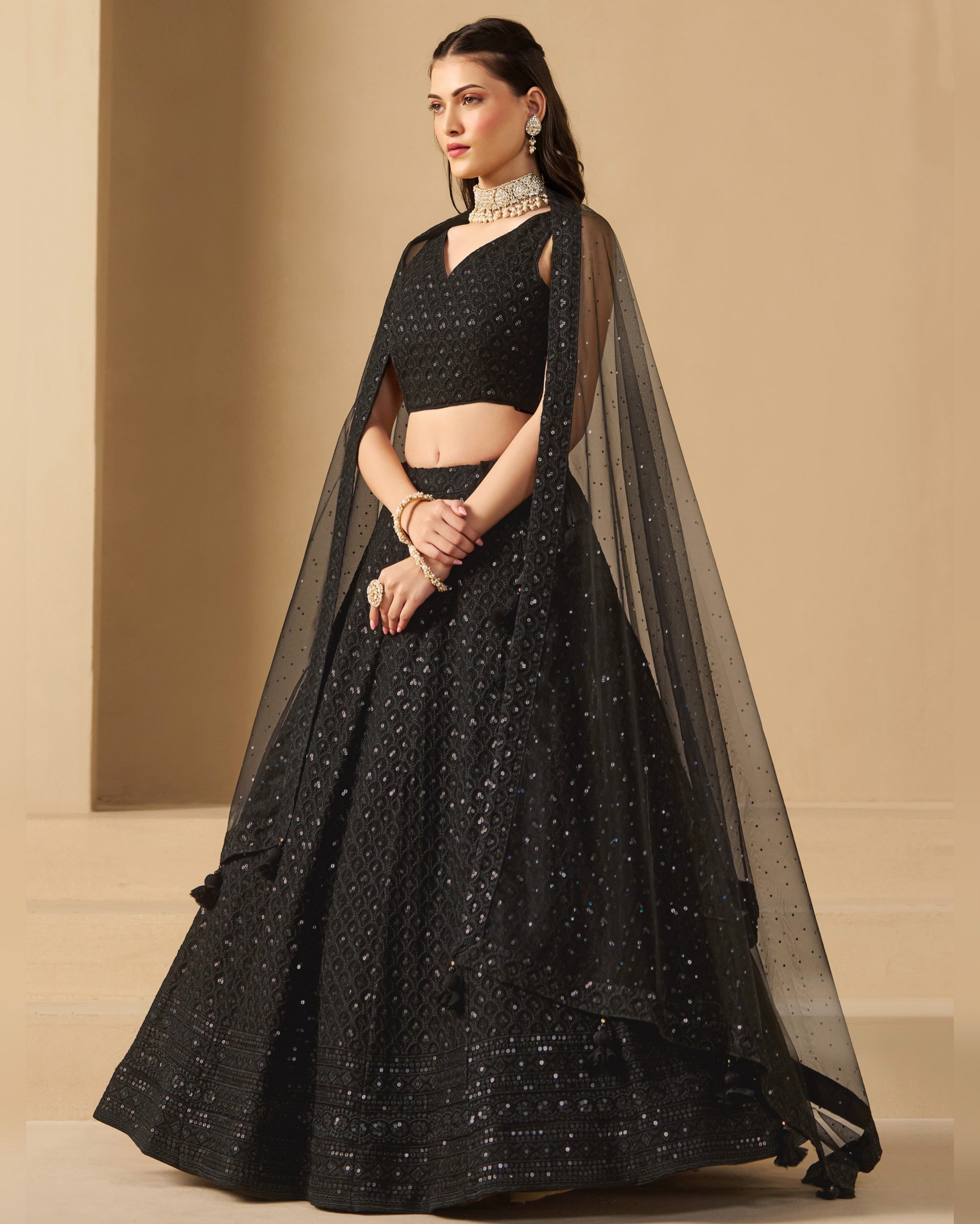 Woman wearing a black embroidered lehenga with a sheer dupatta against a beige background