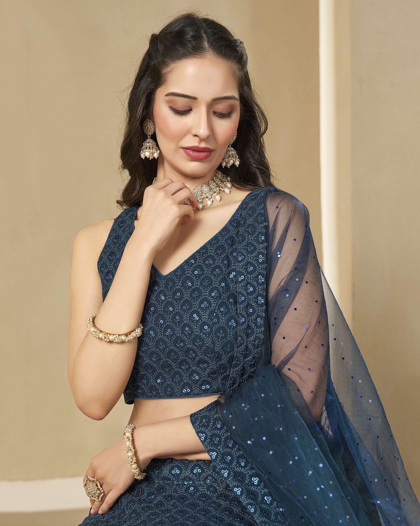 Woman wearing a blue saree with gold jewelry against a beige background