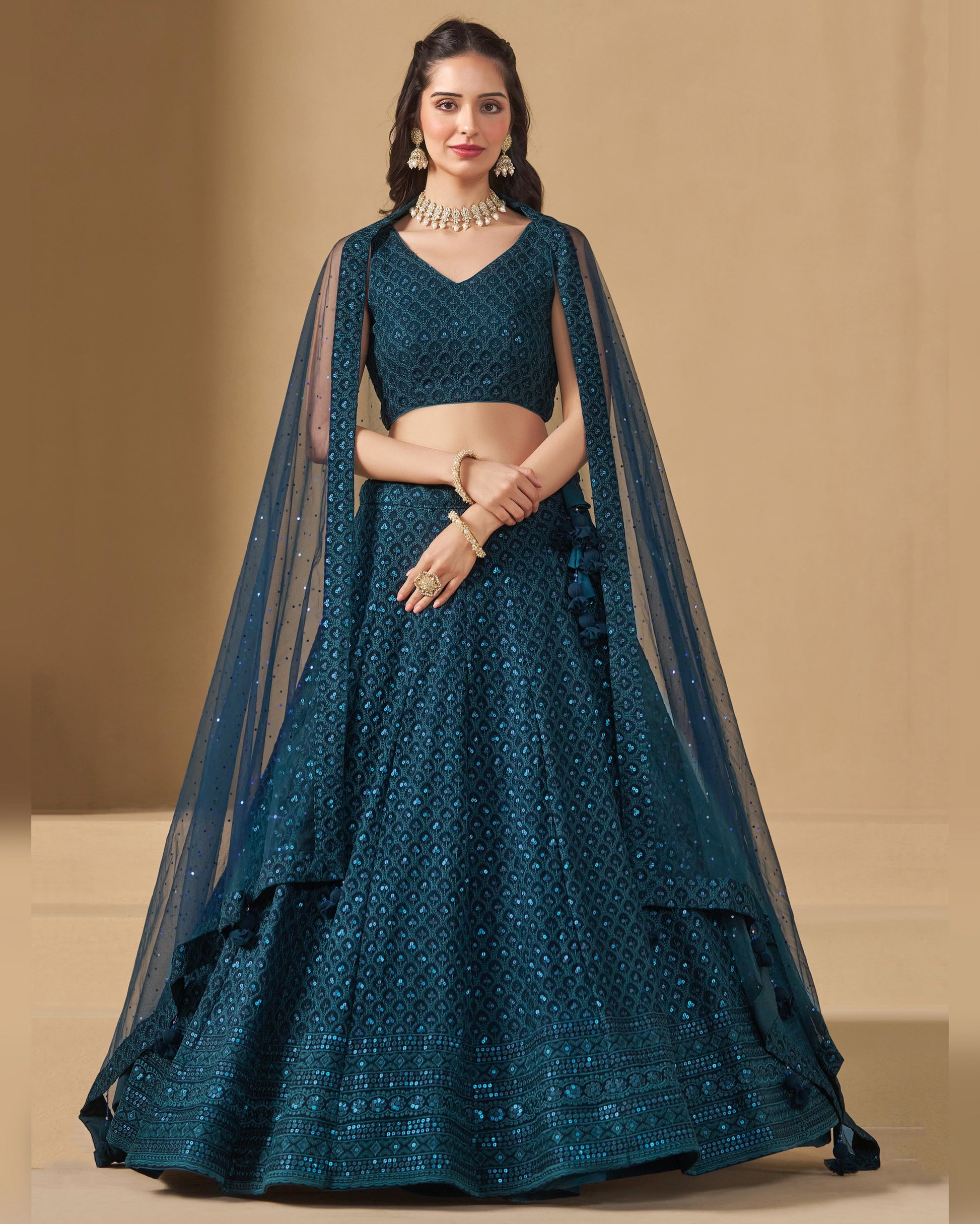 Woman wearing a teal embroidered lehenga with a beige background
