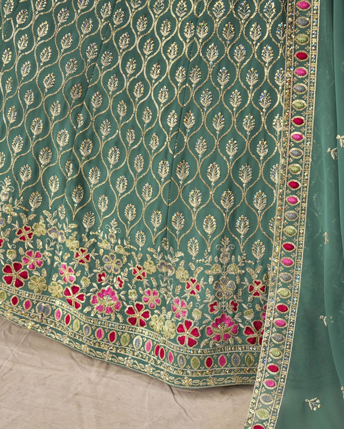 Teal fabric with intricate gold and pink floral embroidery on a beige background