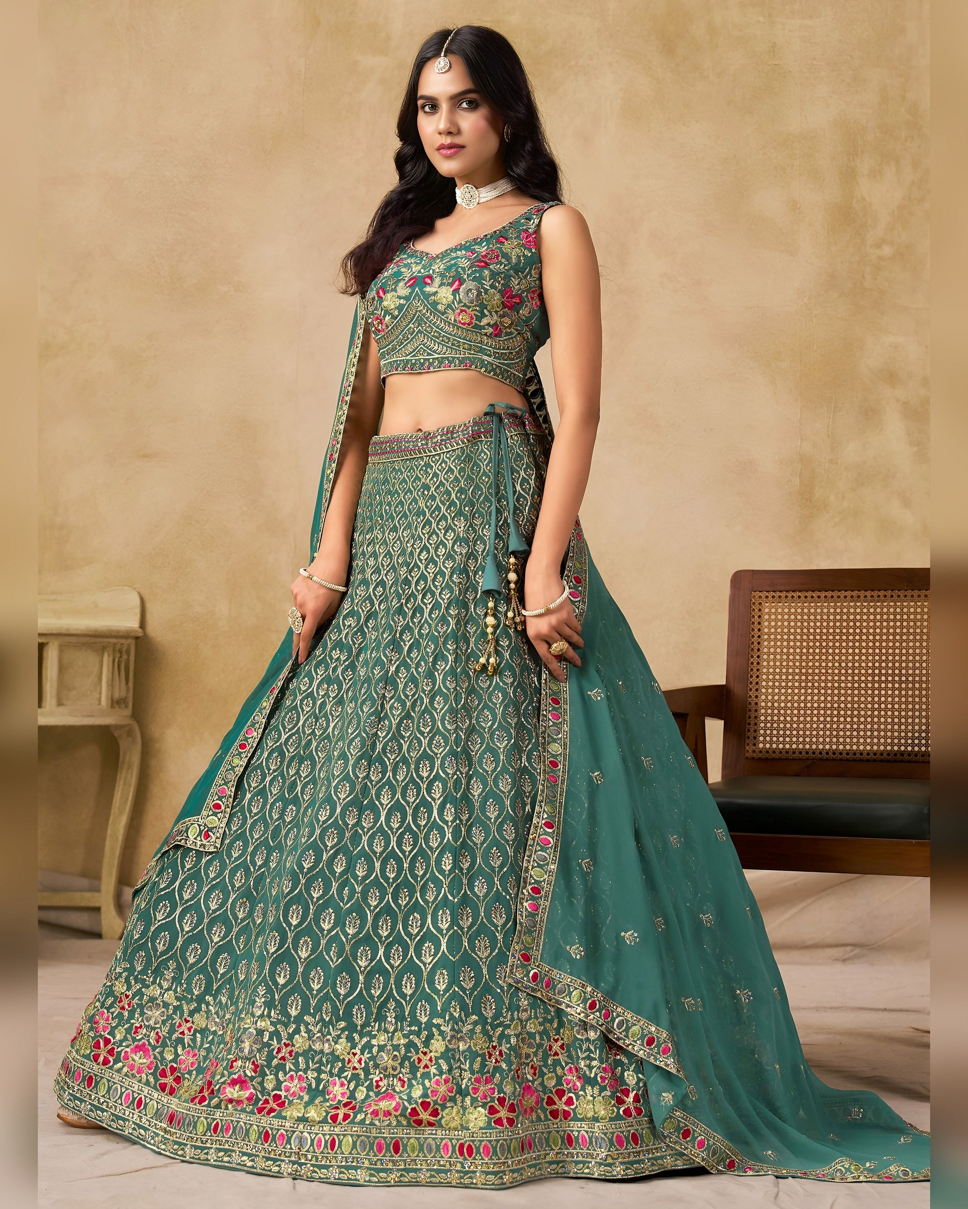 Woman wearing a green embroidered traditional outfit against a beige wall.
