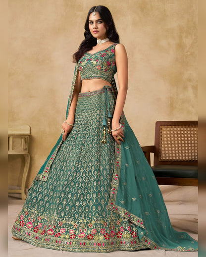 Woman wearing a green embroidered traditional outfit against a beige wall.