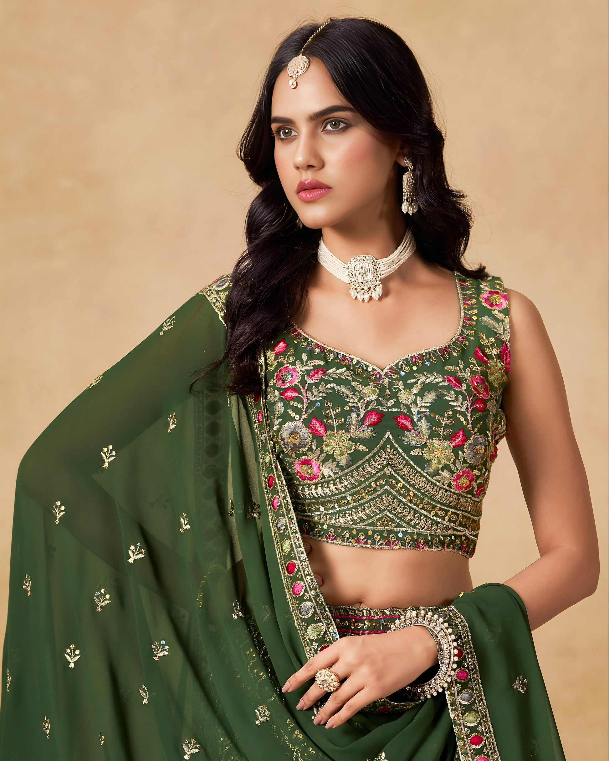 Woman wearing a green embroidered traditional outfit with jewelry on a beige background