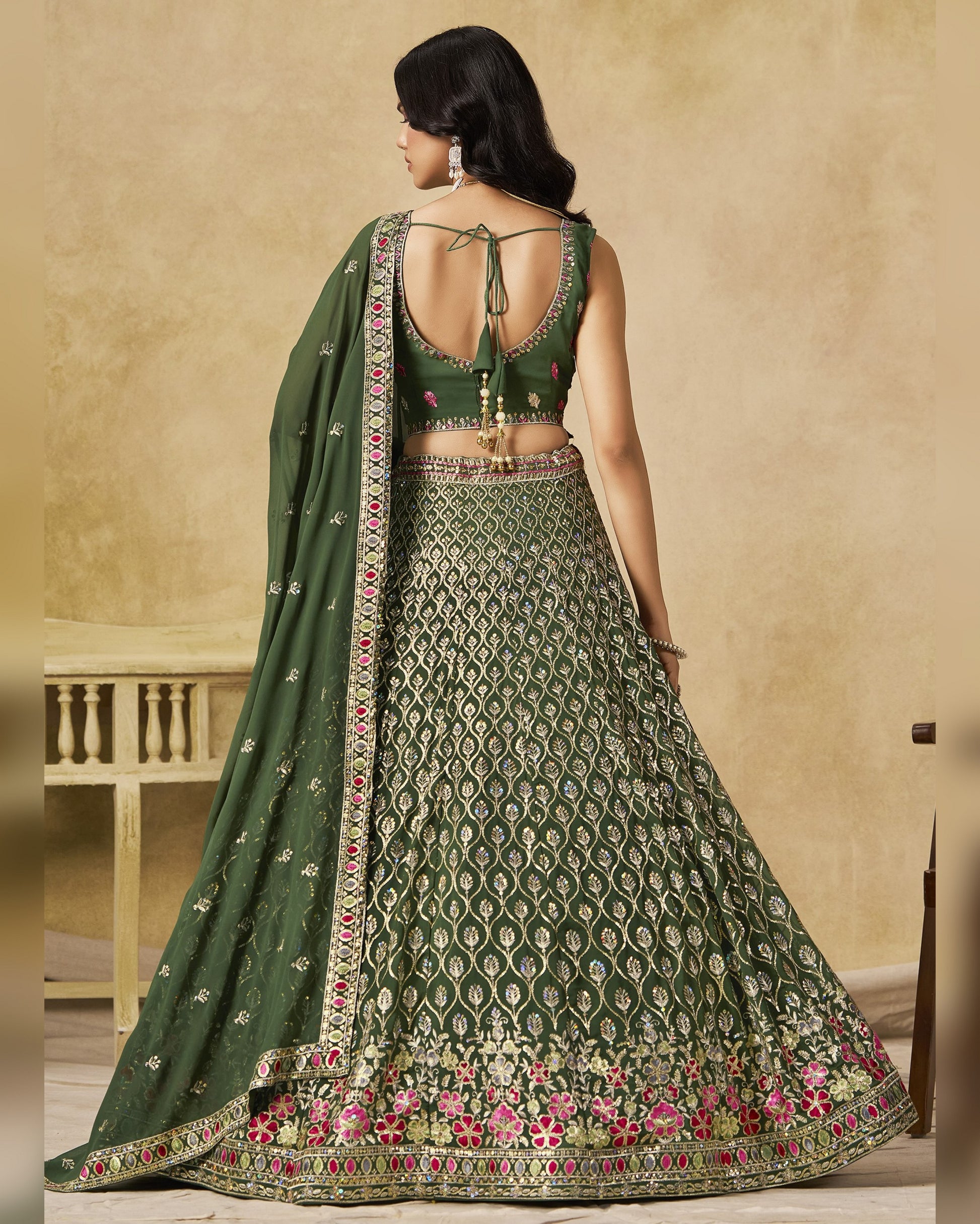 Woman wearing a green embroidered lehenga with a matching dupatta in a neutral setting