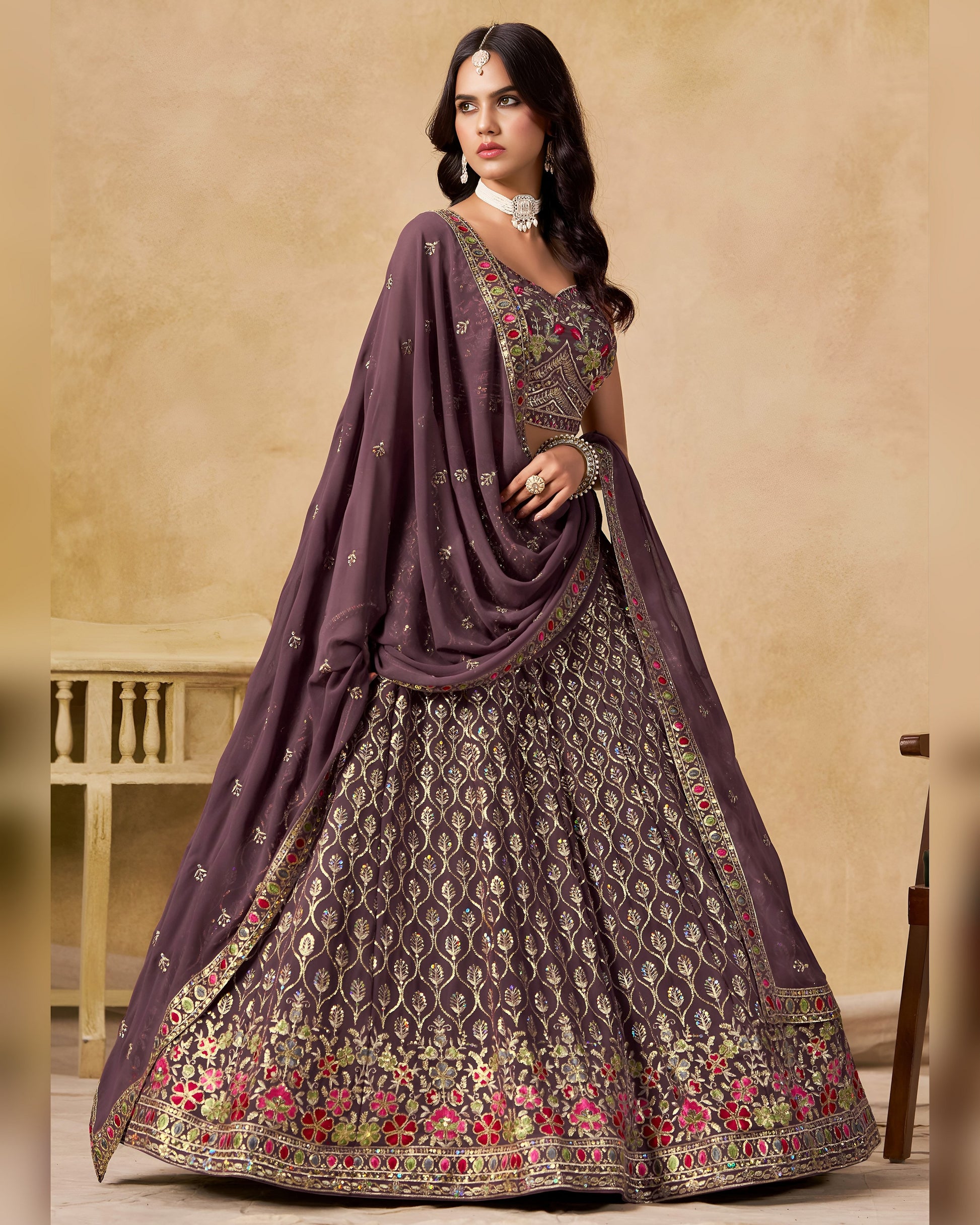 Woman wearing a traditional outfit with a purple dupatta and embroidered skirt on a beige background