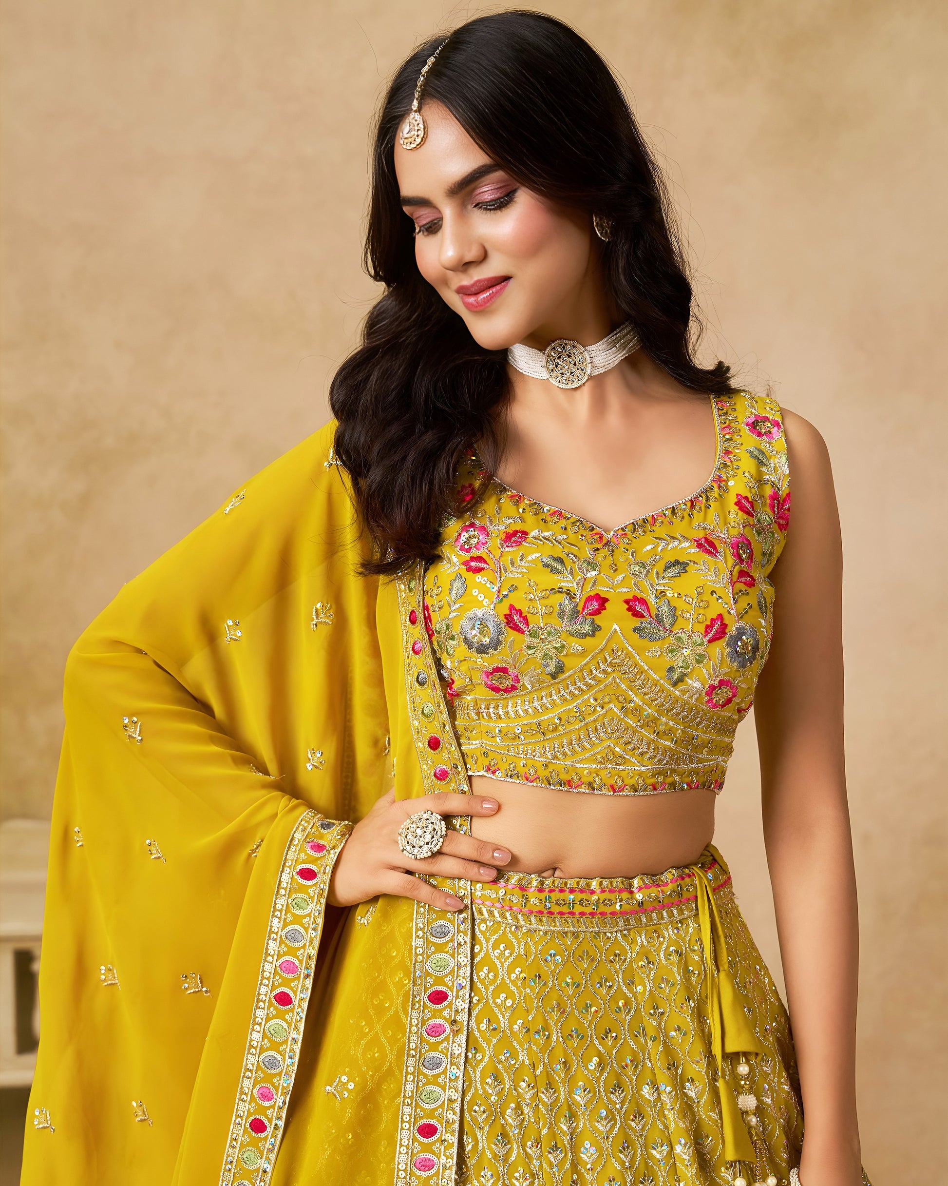 Woman wearing a yellow embroidered traditional outfit against a beige background