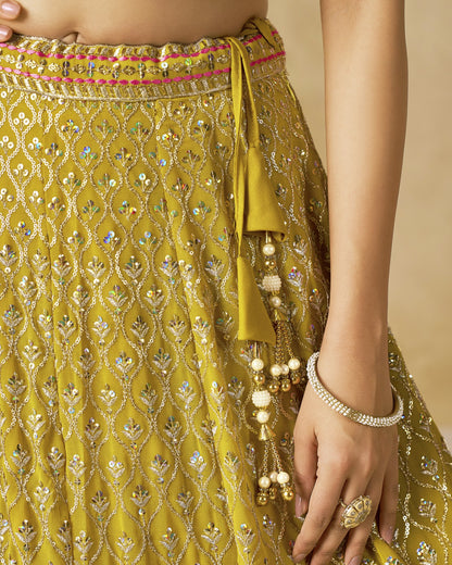 Close-up of a person wearing a yellow embroidered traditional outfit with jewelry on a beige background