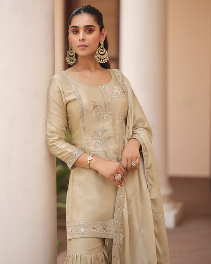 Woman wearing a beige embroidered traditional outfit with jewelry against a neutral background