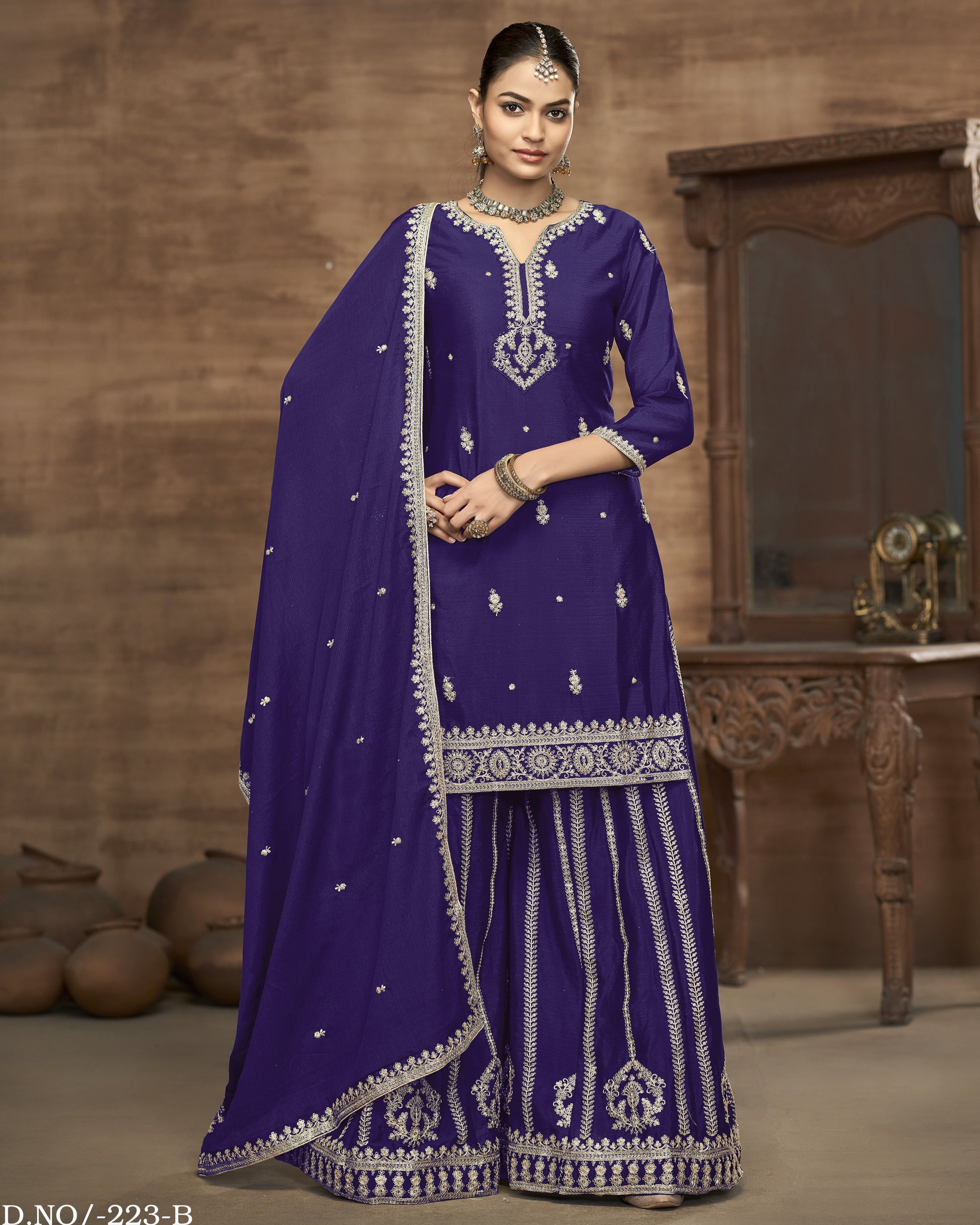 Woman wearing a traditional purple outfit with intricate white embroidery in a warm-toned room.