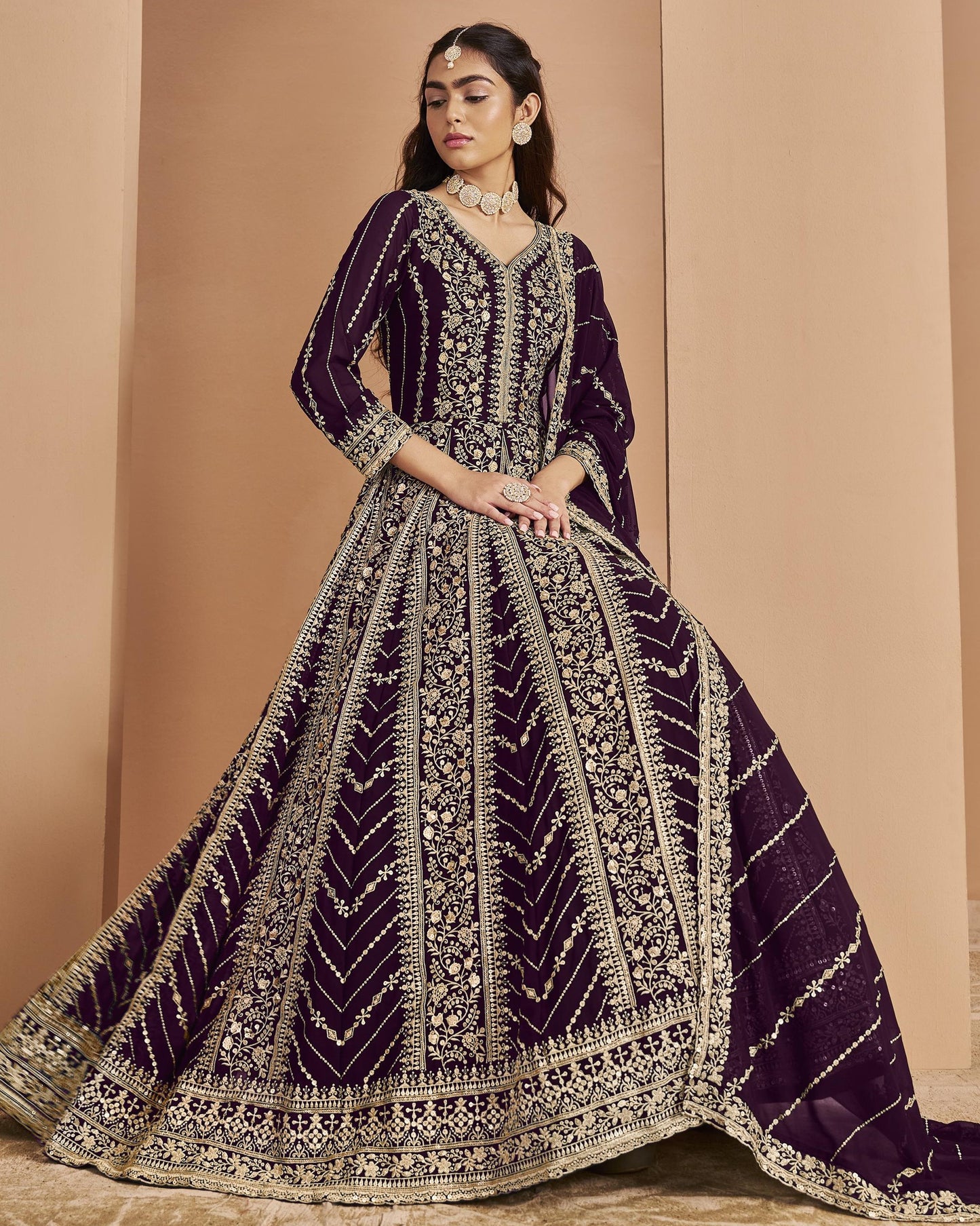 Woman wearing a purple and gold embroidered traditional outfit against a beige background