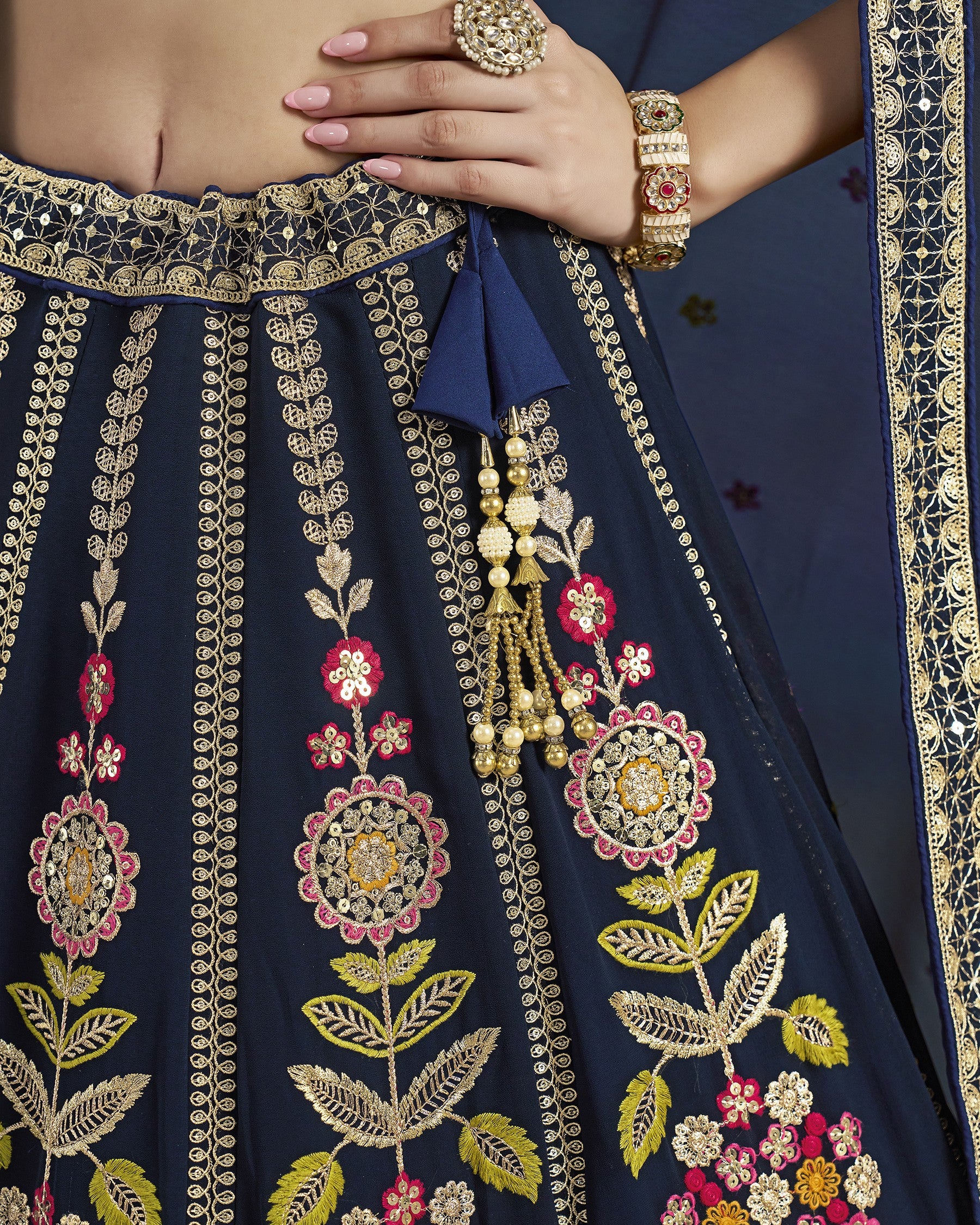 Navy blue embroidered saree with gold and pink floral patterns, held by a hand.