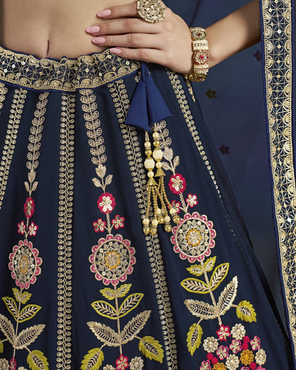 Navy blue embroidered saree with gold and pink floral patterns, held by a hand.