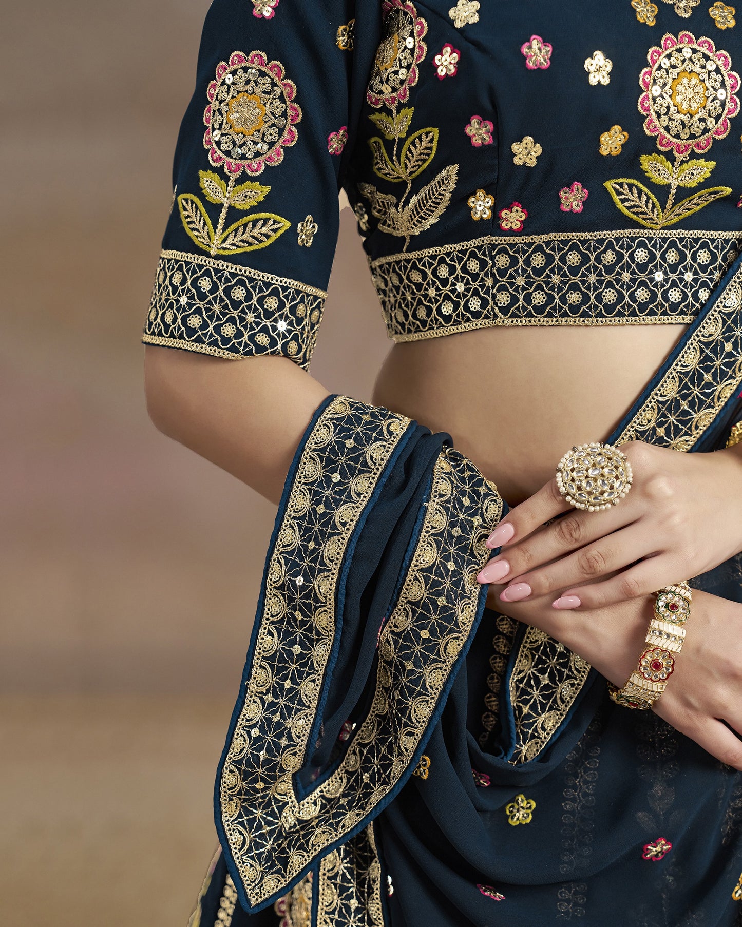 Navy blue embroidered saree with gold details and jewelry on a blurred background