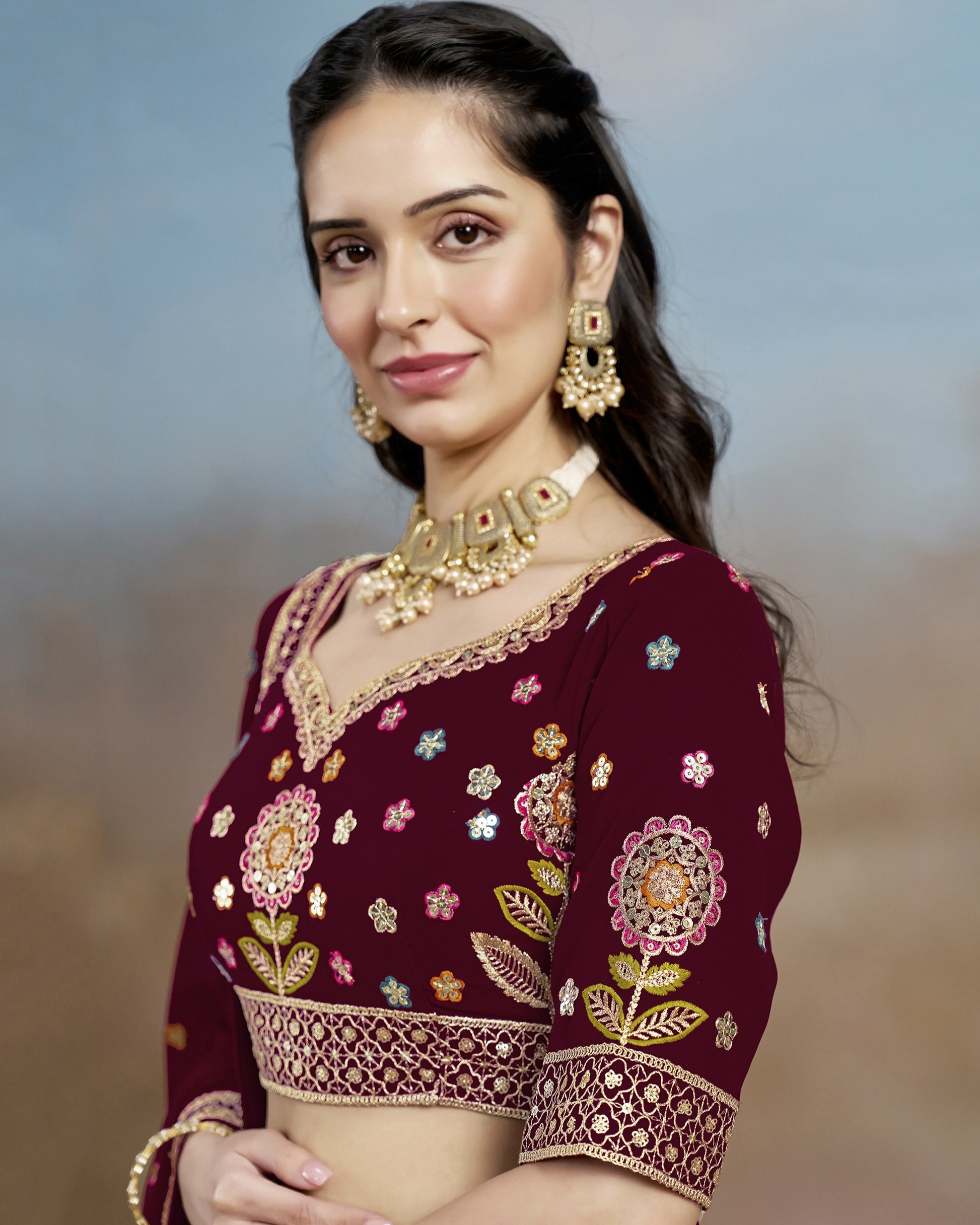 Woman wearing a maroon embroidered blouse with floral patterns against a blurred natural background
