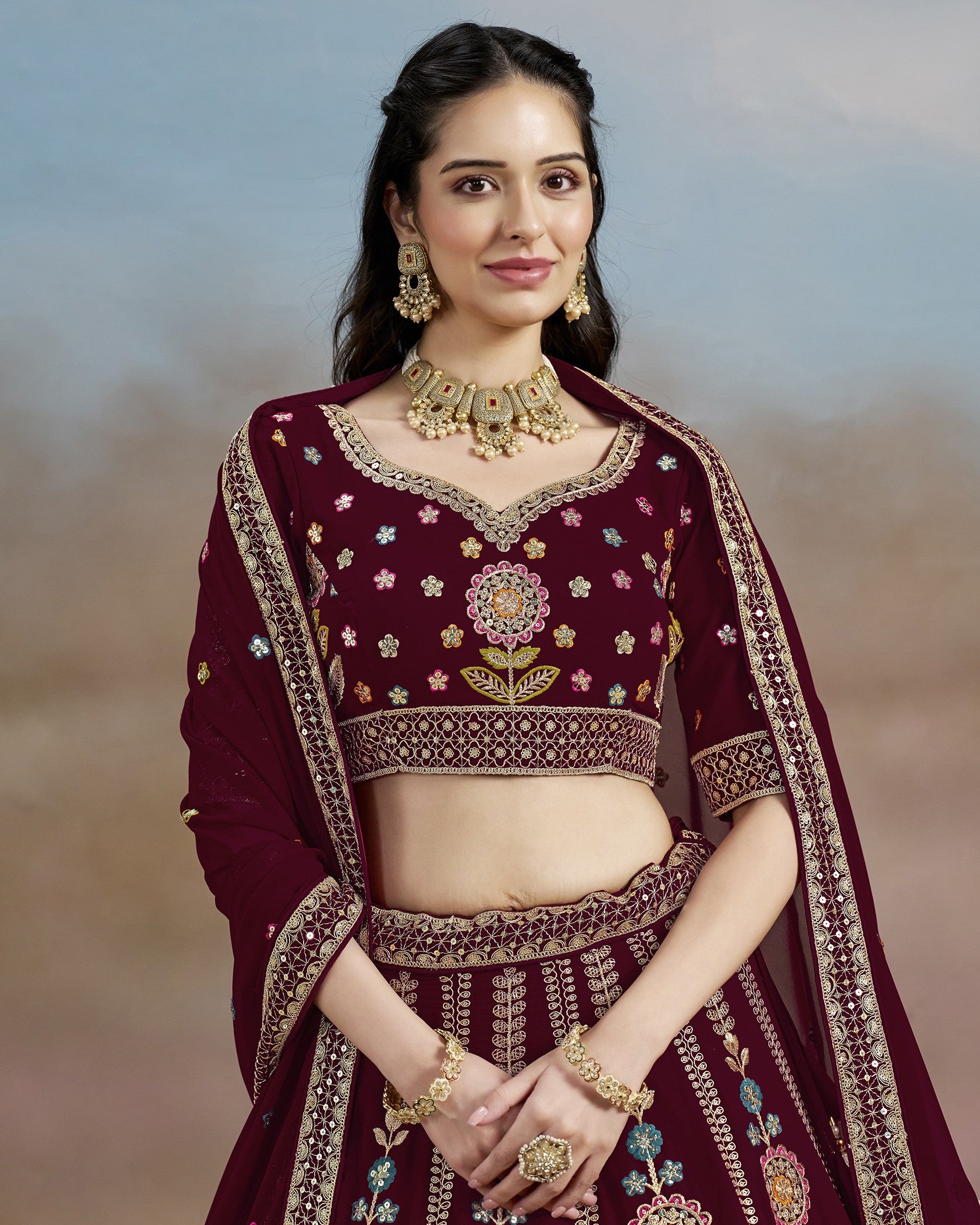 Woman in a maroon embroidered traditional outfit with jewelry against a blurred natural background