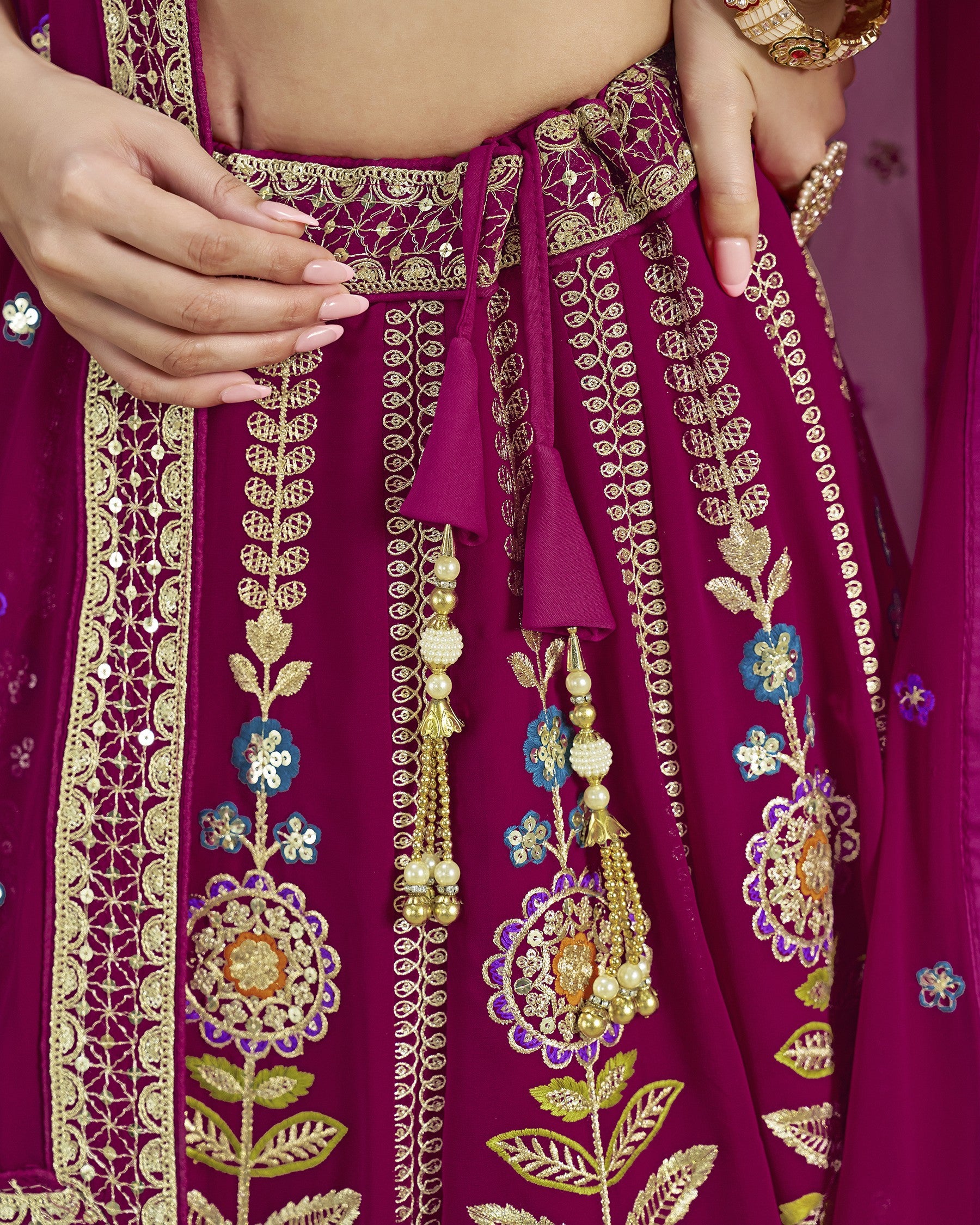 Close-up of a maroon traditional outfit with gold embroidery and floral patterns.
