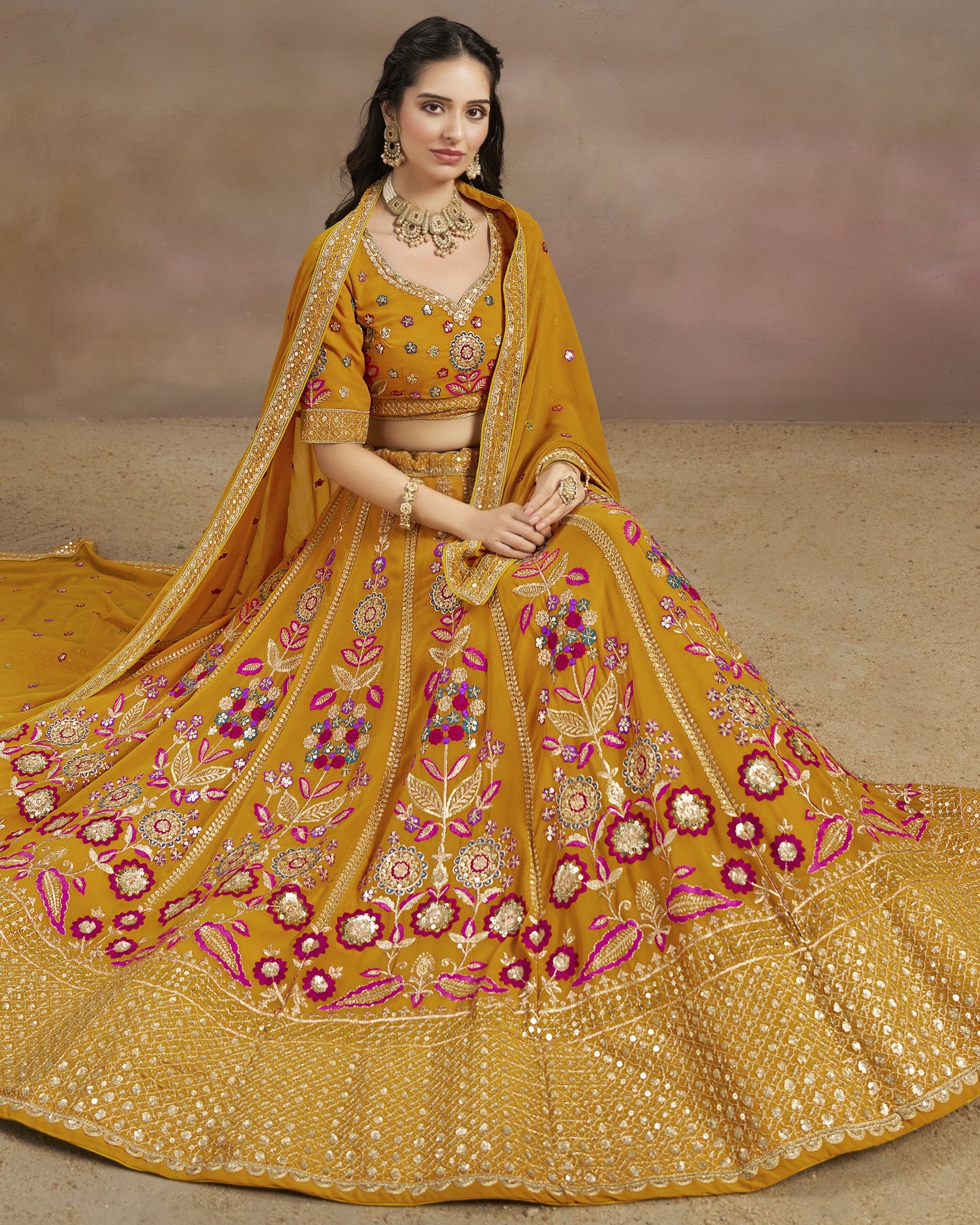 Woman wearing a traditional yellow embroidered outfit with a matching dupatta on a neutral background