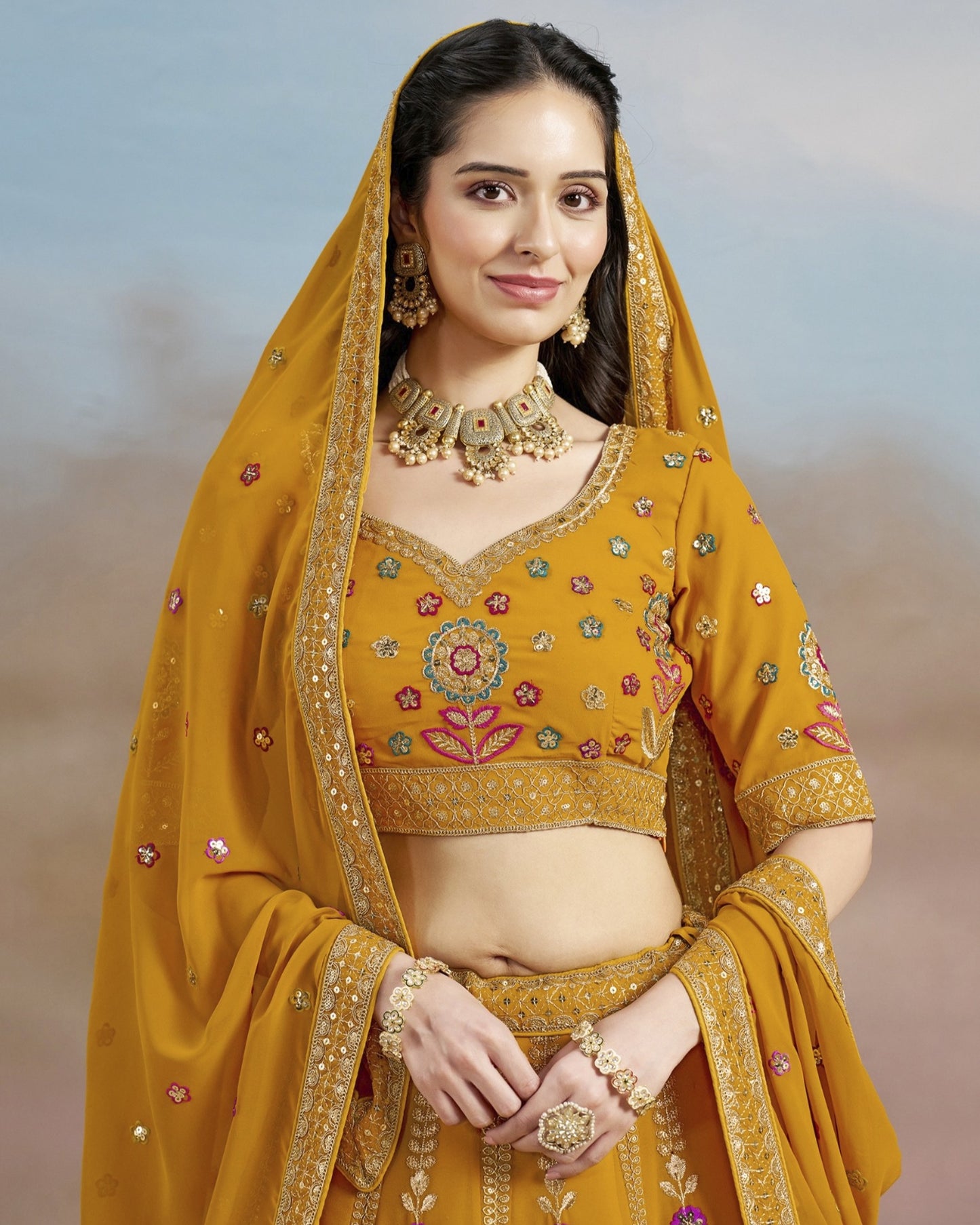 Woman wearing a yellow traditional outfit with intricate designs and jewelry against a neutral background