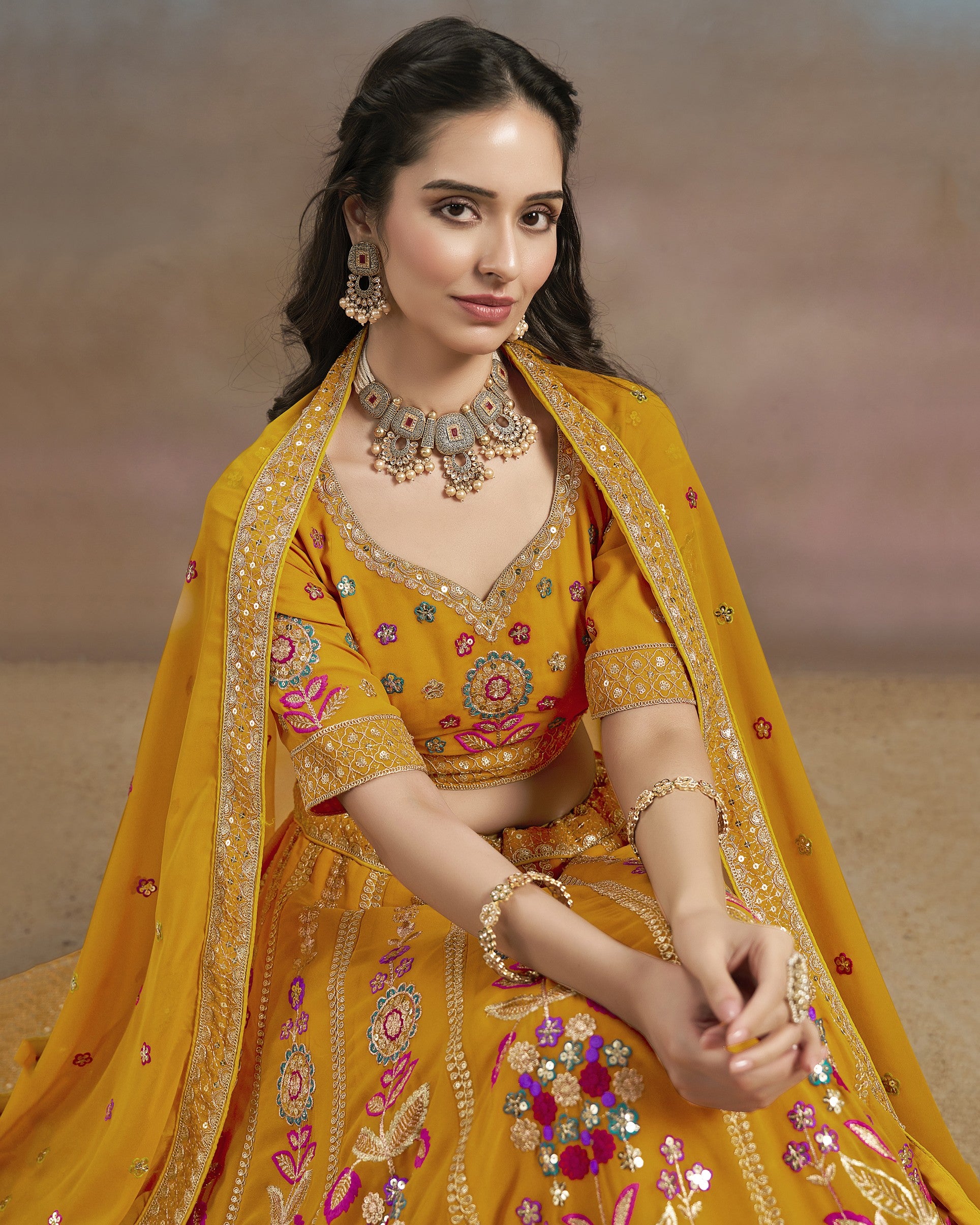Woman in a yellow embroidered traditional outfit with jewelry against a neutral background