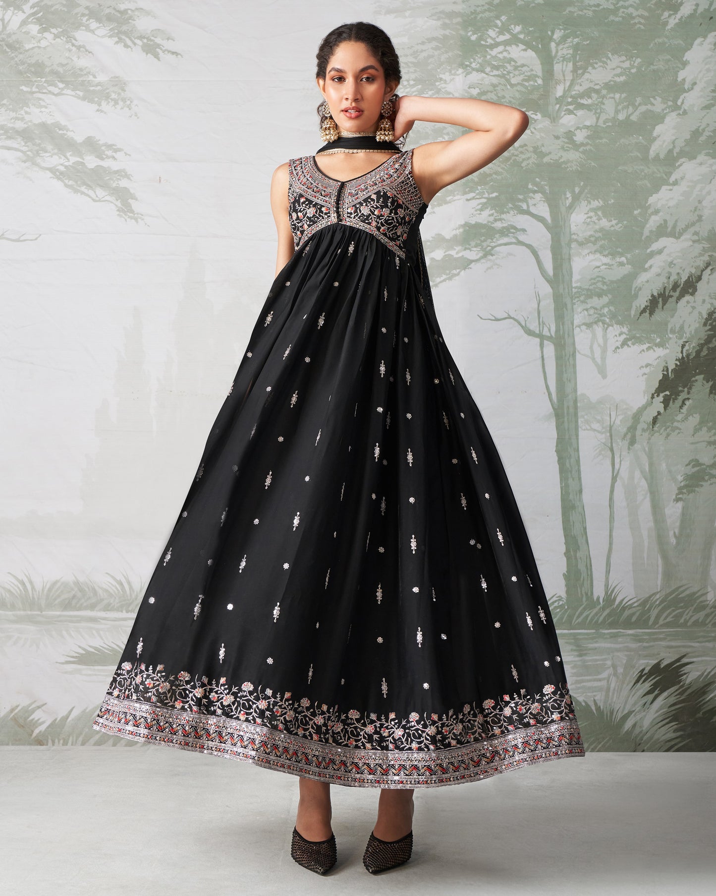 Woman wearing a black dress with intricate patterns against a nature-themed background