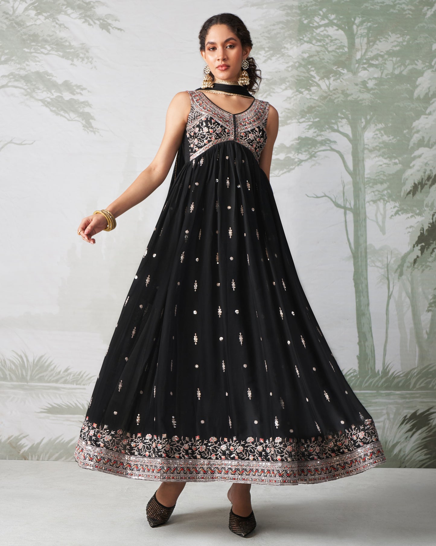 Woman wearing a black dress with floral patterns against a nature-themed background