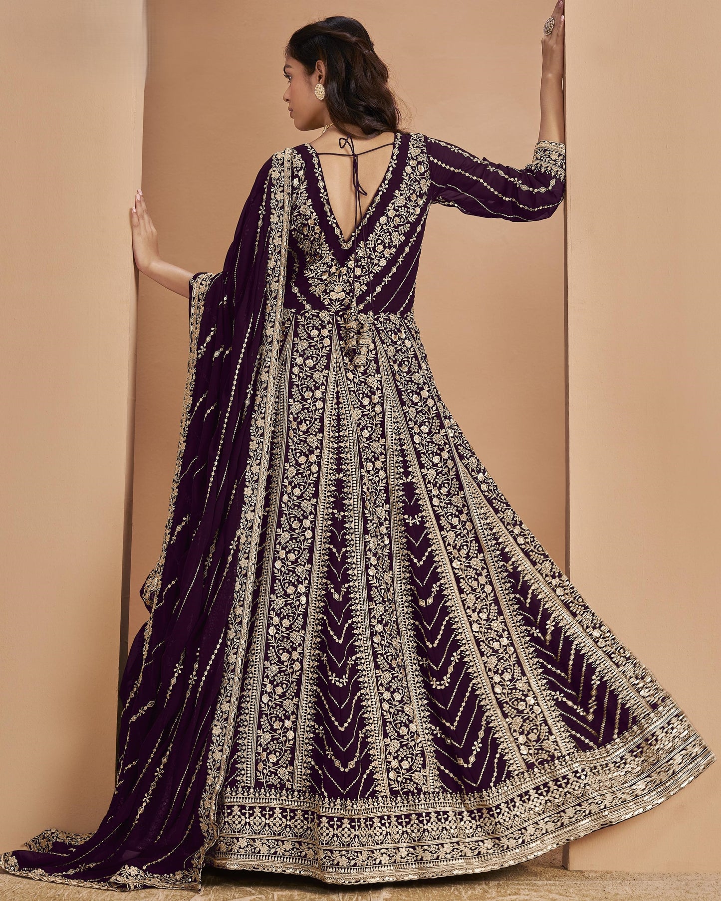 Woman wearing a purple and gold embroidered traditional outfit against a beige background