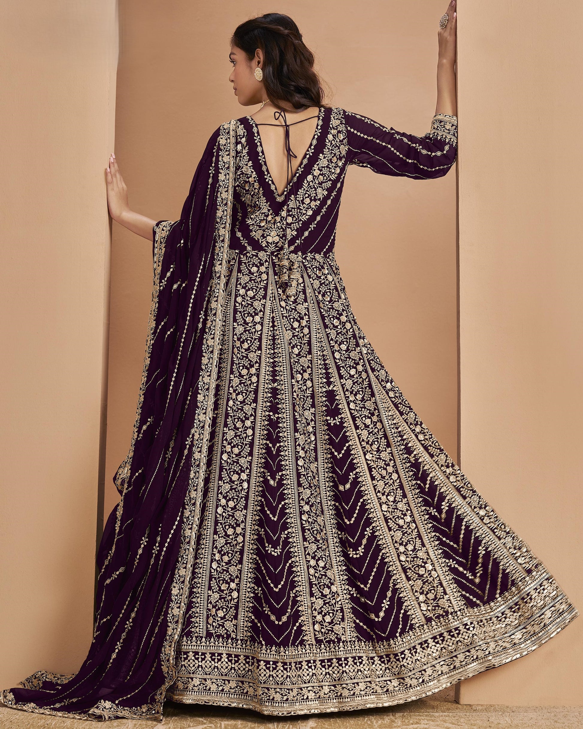 Woman wearing a purple and gold embroidered traditional outfit against a beige background