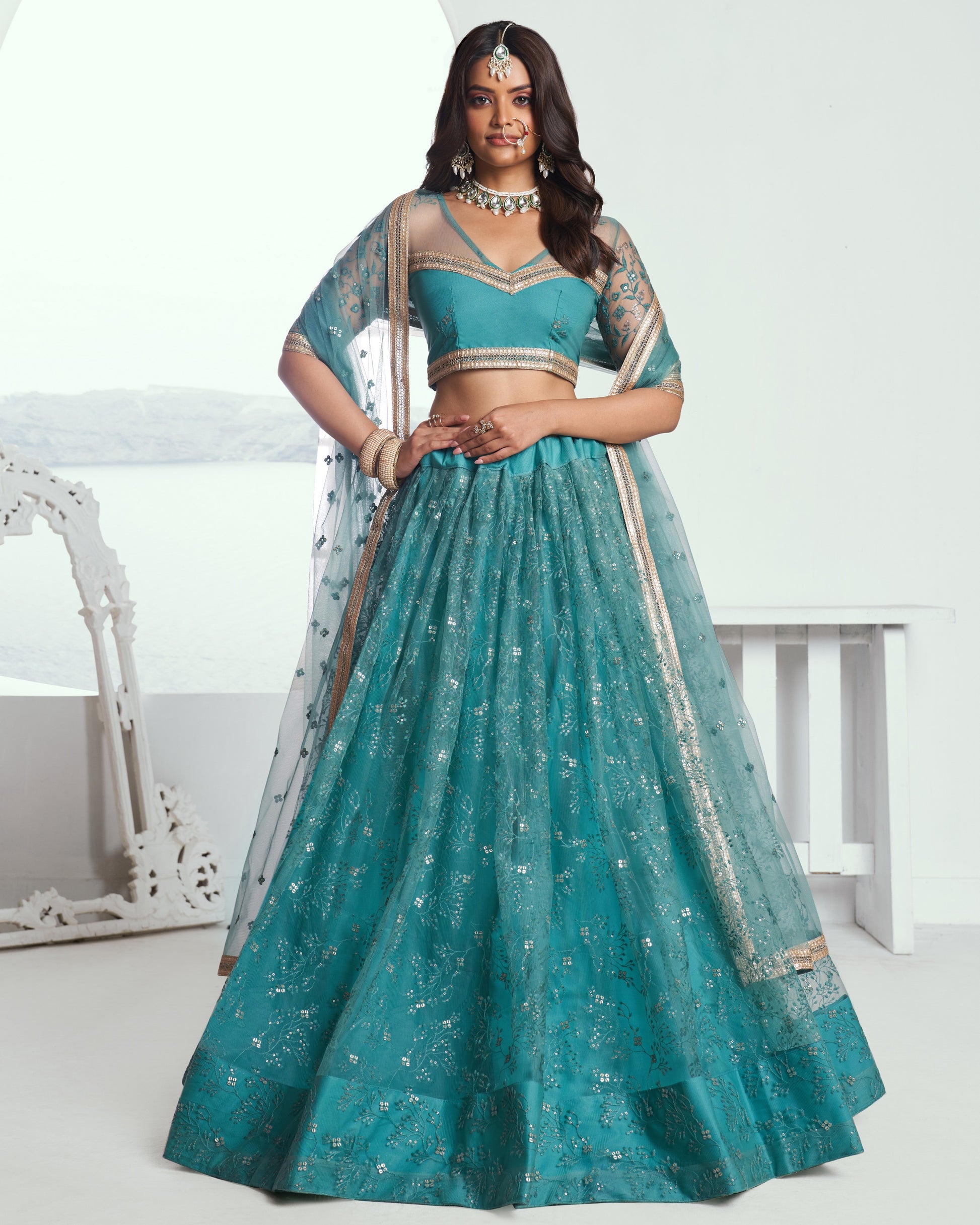 Woman wearing a teal traditional outfit with silver details on a white background