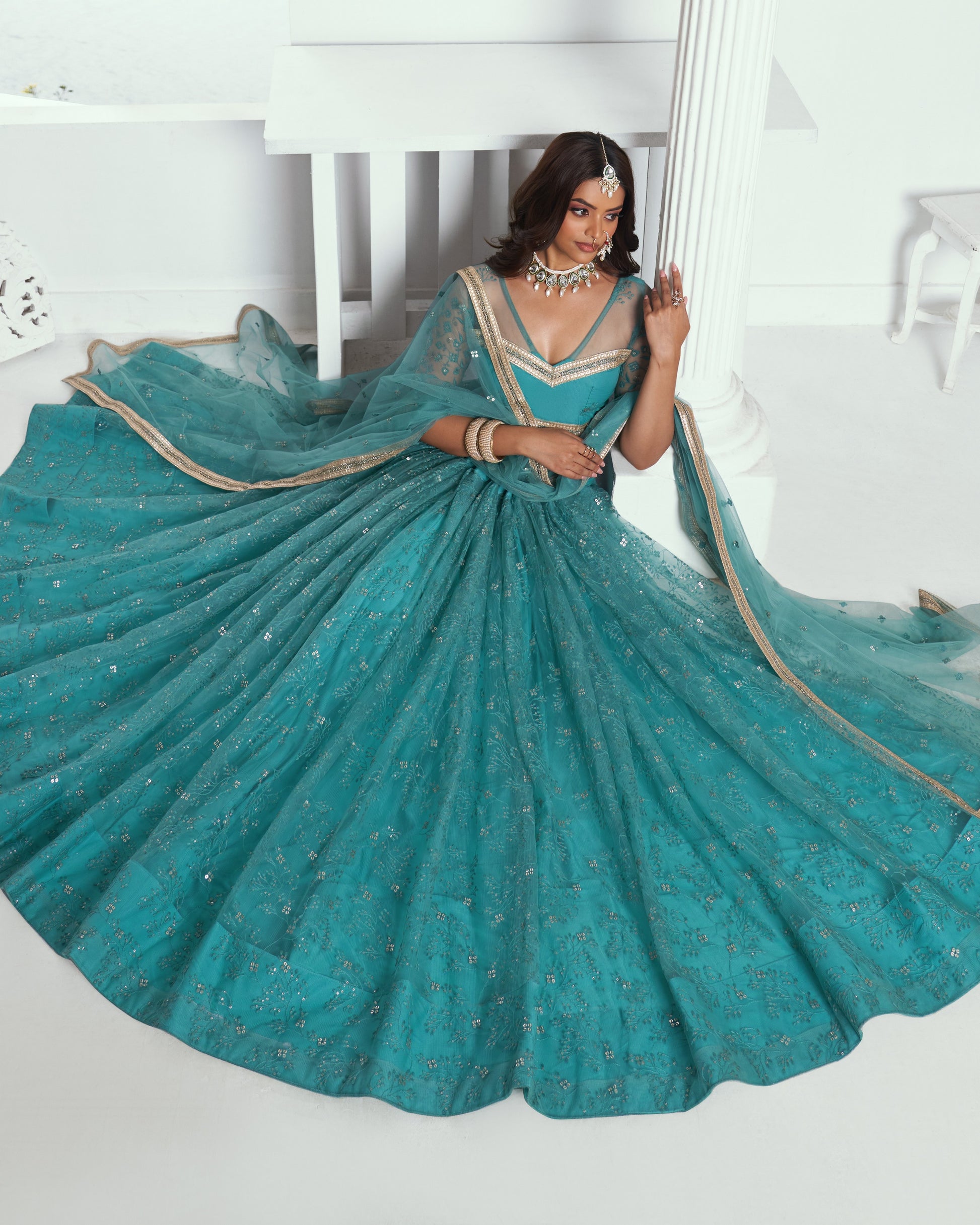 Woman in a teal saree with gold details against a white background