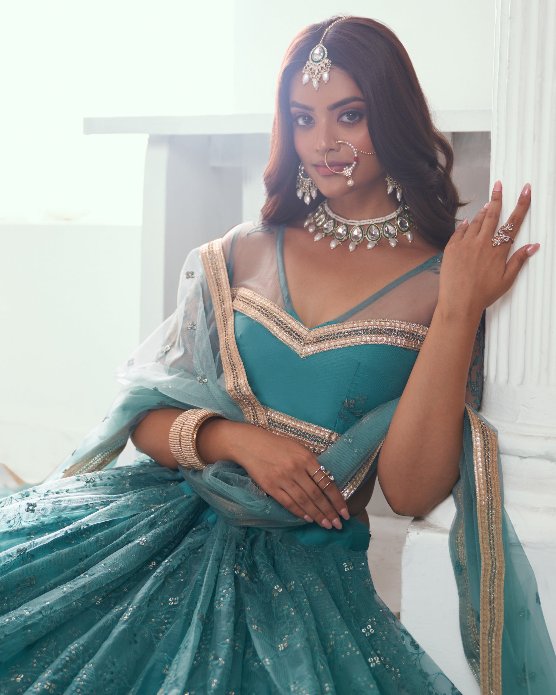 Woman in a teal traditional outfit with gold details indoors.