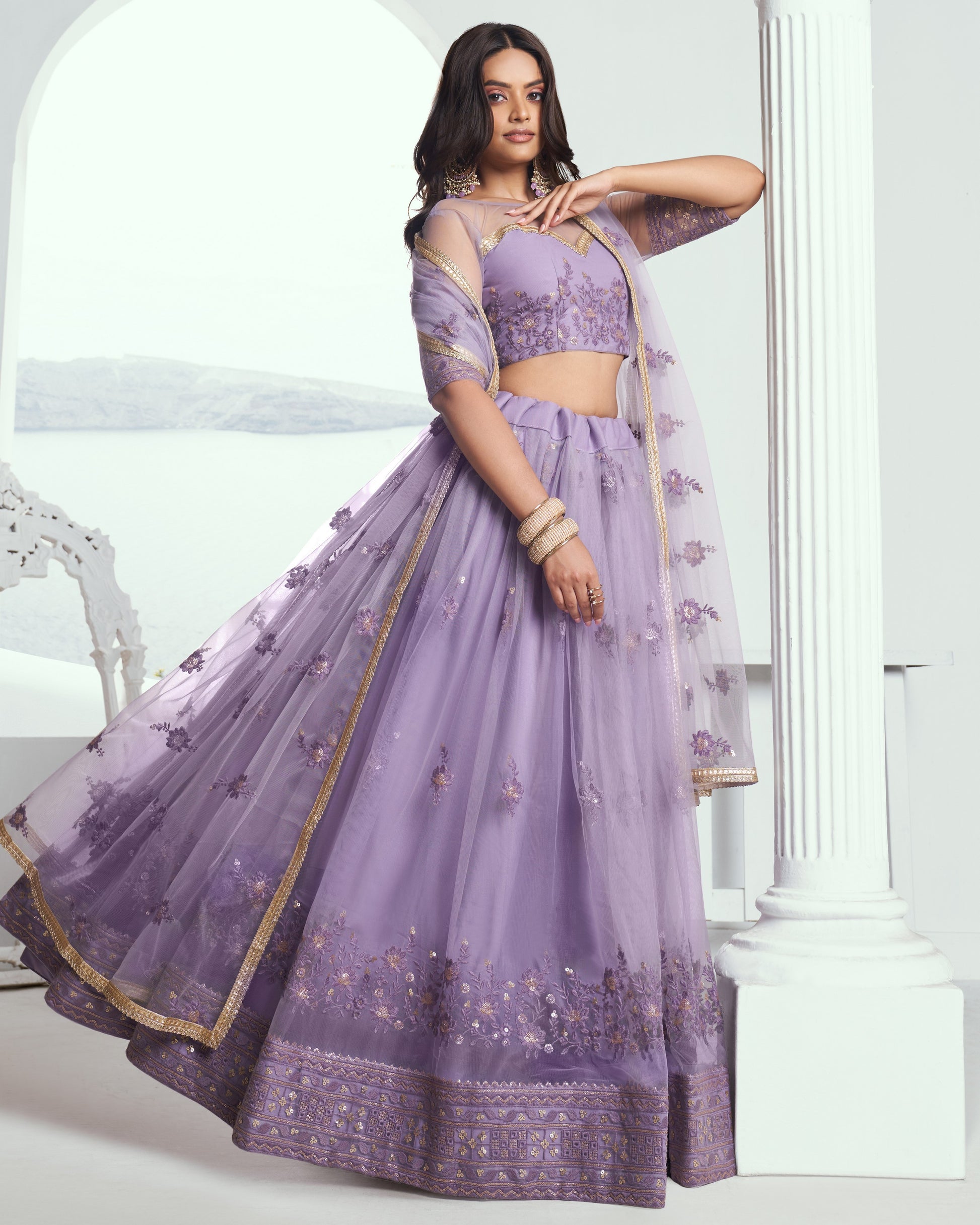 Woman wearing a purple embroidered lehenga in a white room