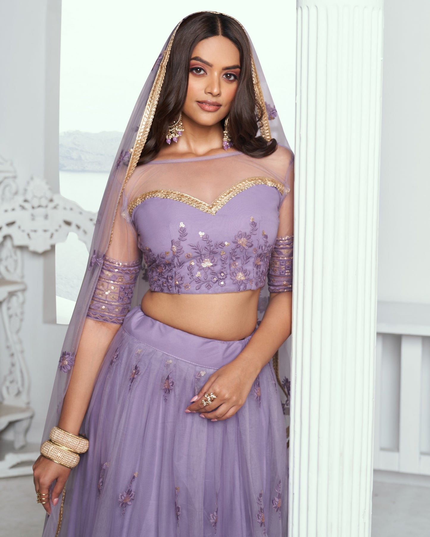 Woman wearing a purple embroidered outfit with a matching dupatta in a white room.
