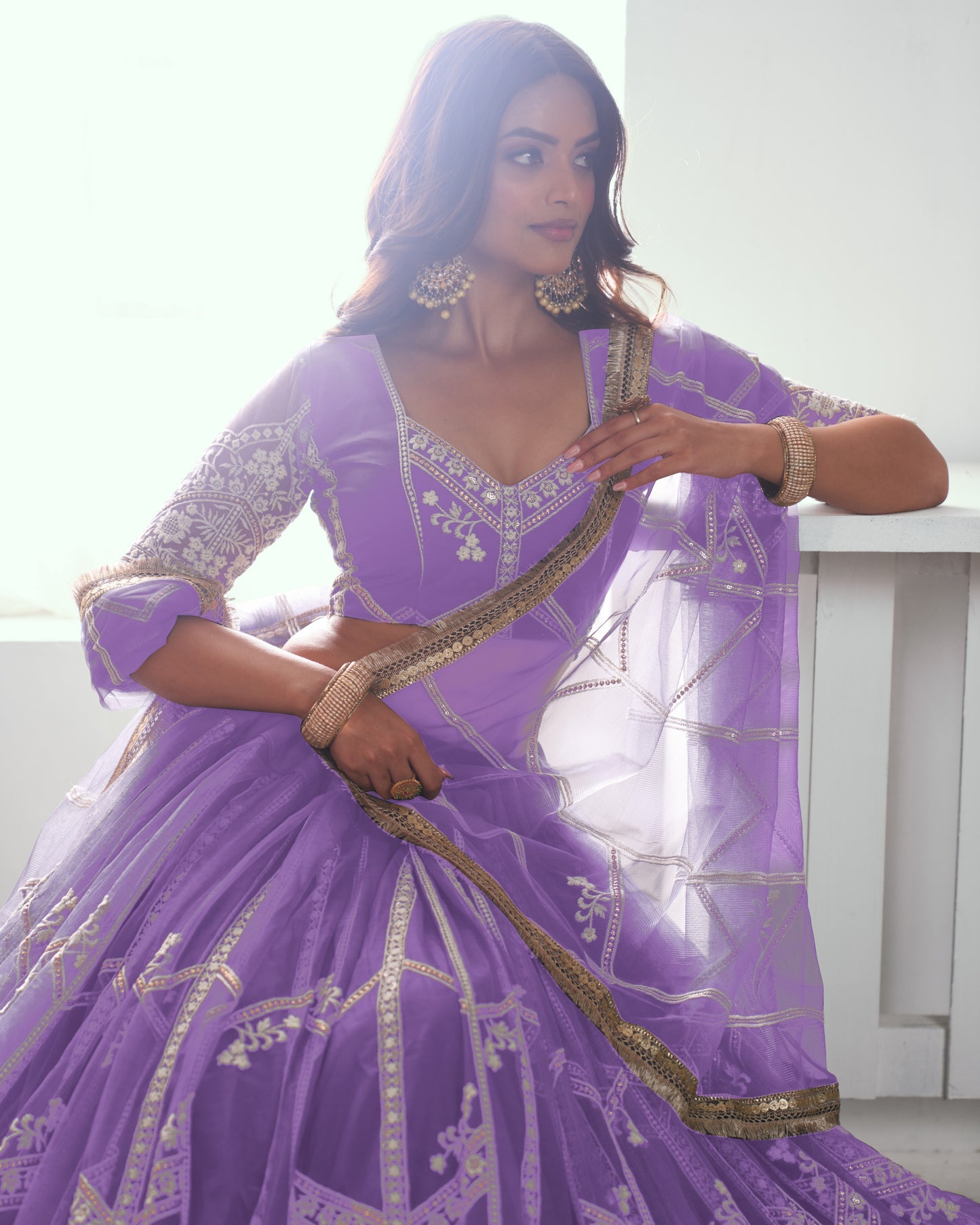 Woman in a purple traditional outfit with gold accents, sitting on a white surface.