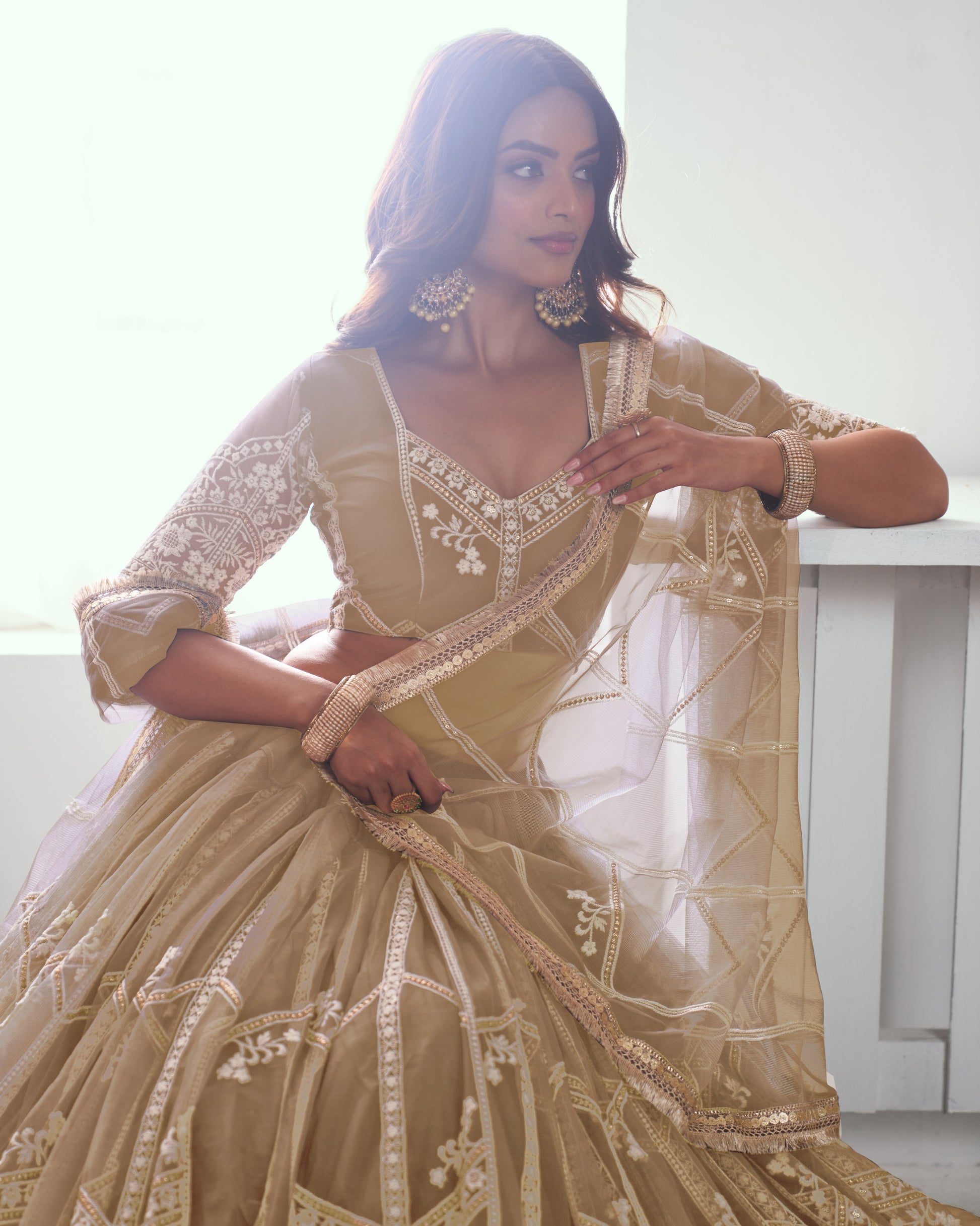 Woman in a traditional beige embroidered outfit sitting indoors.