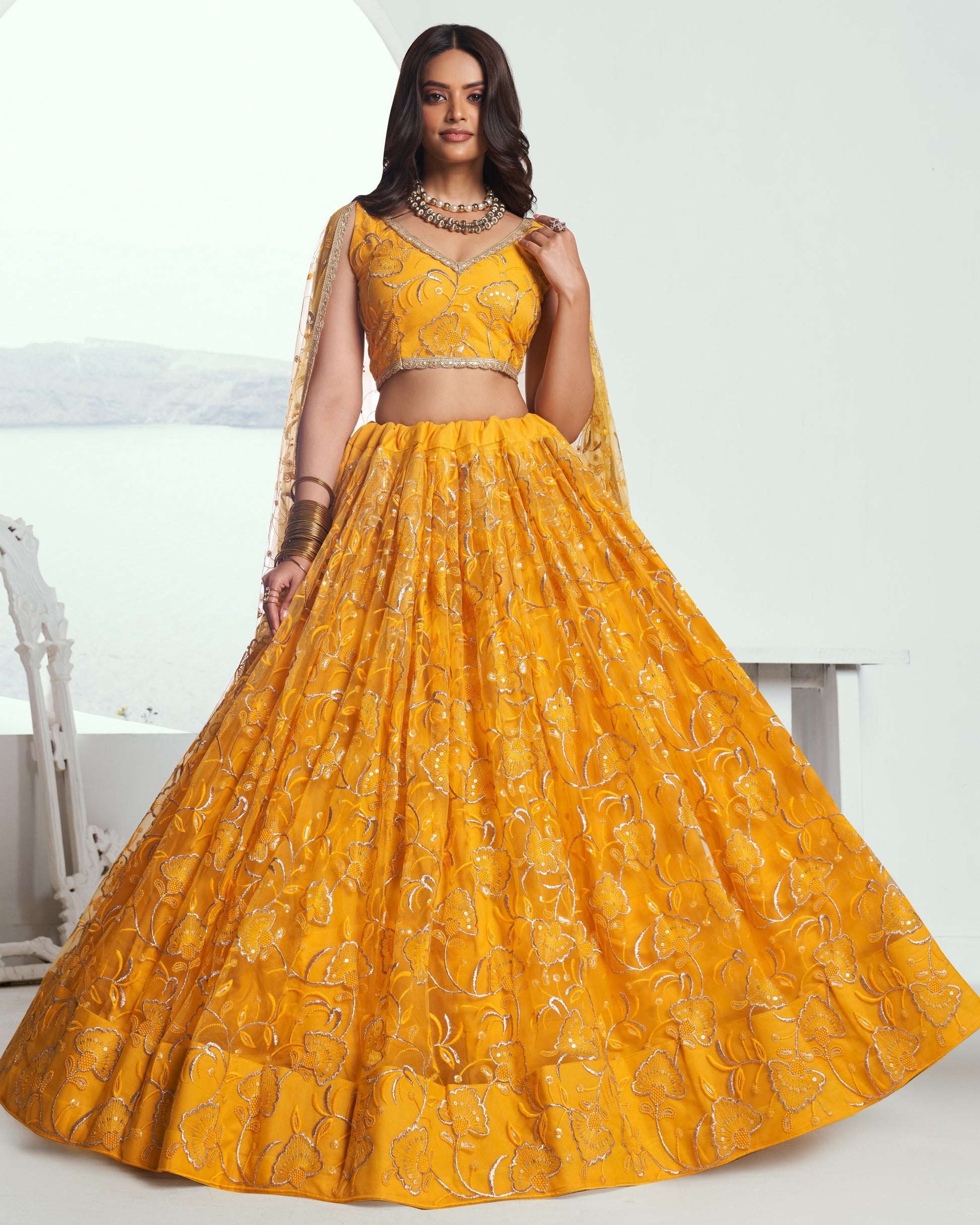 Woman wearing a yellow embroidered lehenga with a white background