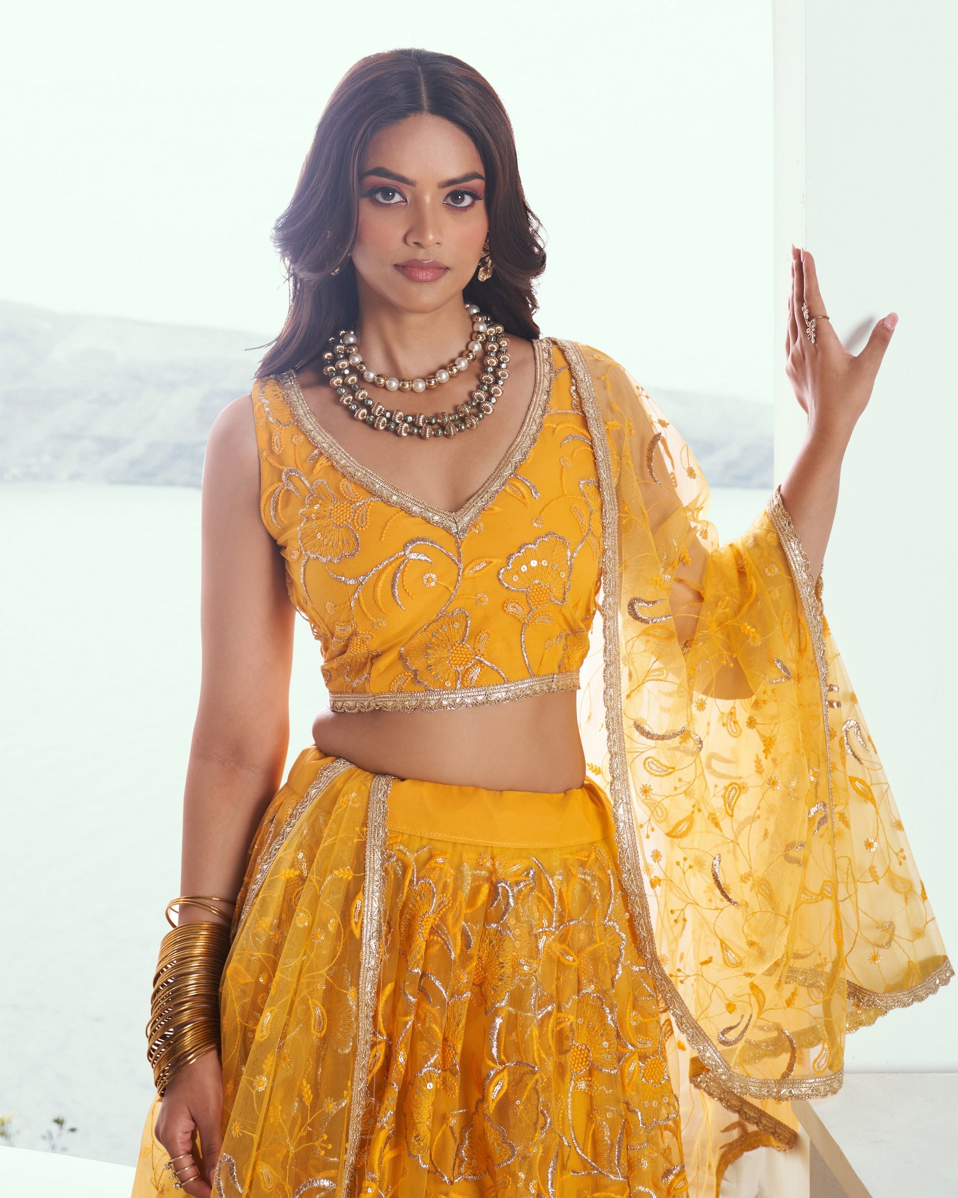 Woman wearing a yellow traditional outfit with intricate designs against a white background