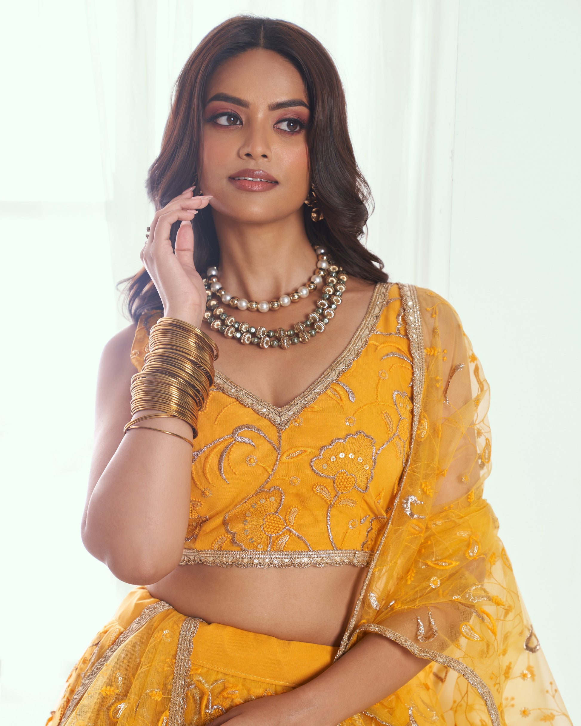 Woman wearing a yellow embroidered traditional outfit with gold jewelry on a white background