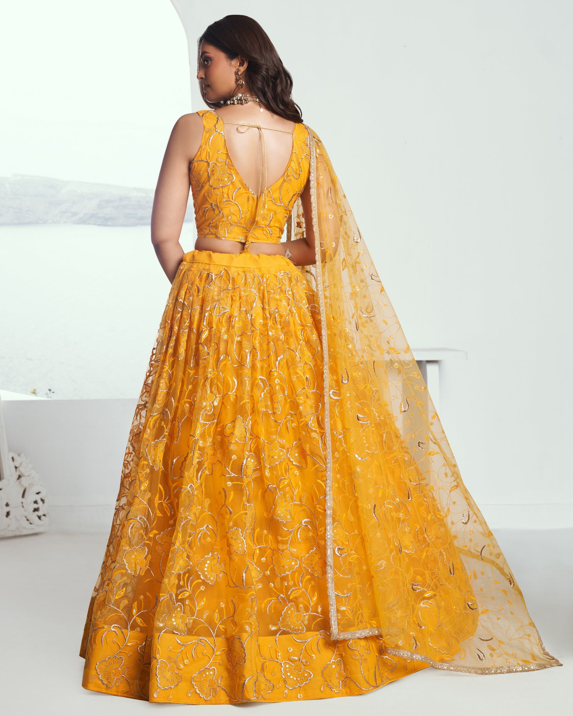 Woman wearing a yellow embroidered lehenga with a white background