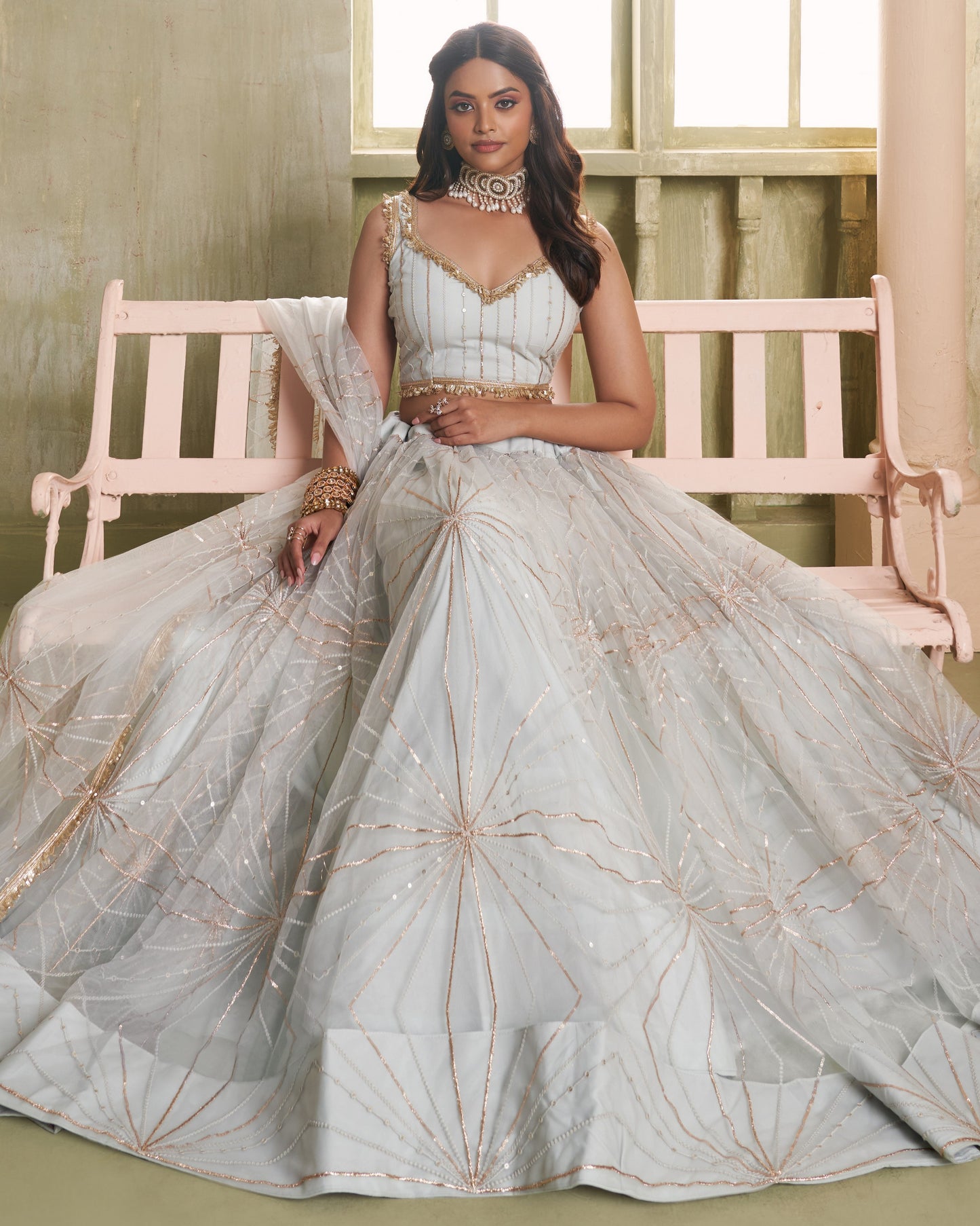 Woman in a light blue embroidered traditional outfit sitting on a pink bench.