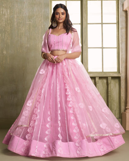 Woman wearing a pink traditional outfit with a matching skirt in a room with wooden walls.