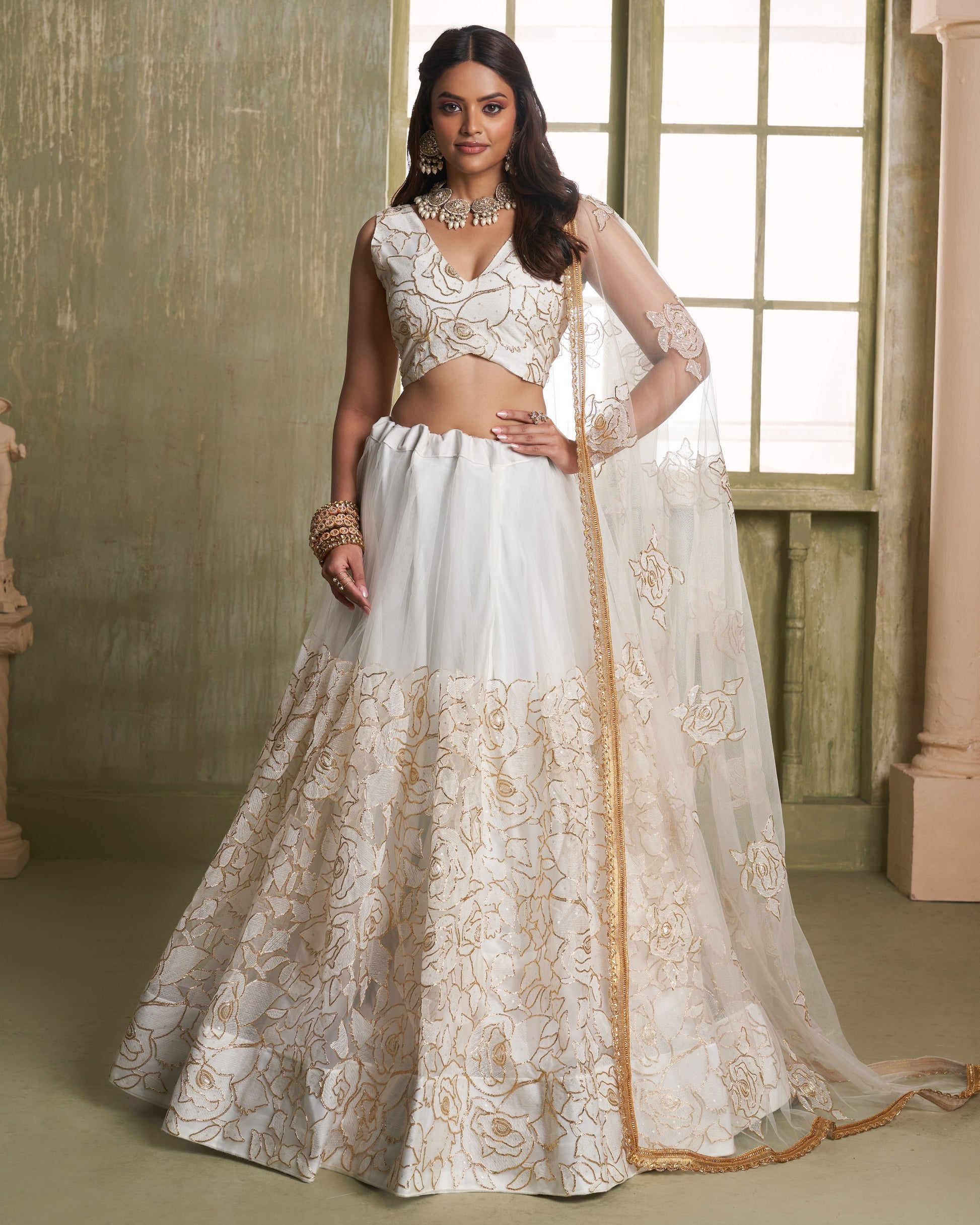 Woman wearing a white and gold embroidered traditional outfit indoors.