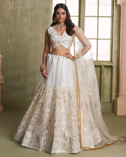 Woman wearing a white and gold embroidered traditional outfit indoors.