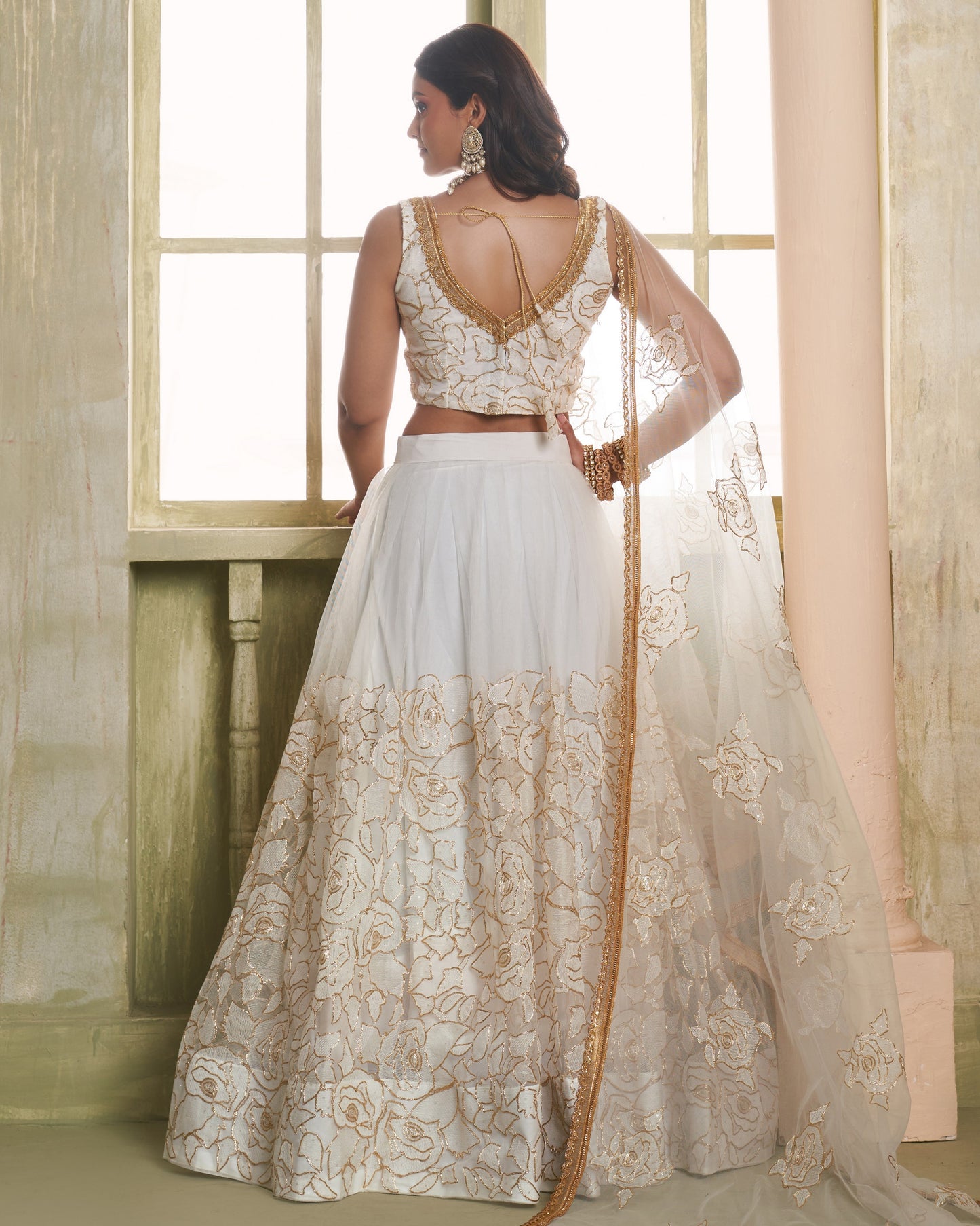 Woman wearing a white and gold traditional outfit with a flowing skirt in a softly lit room.