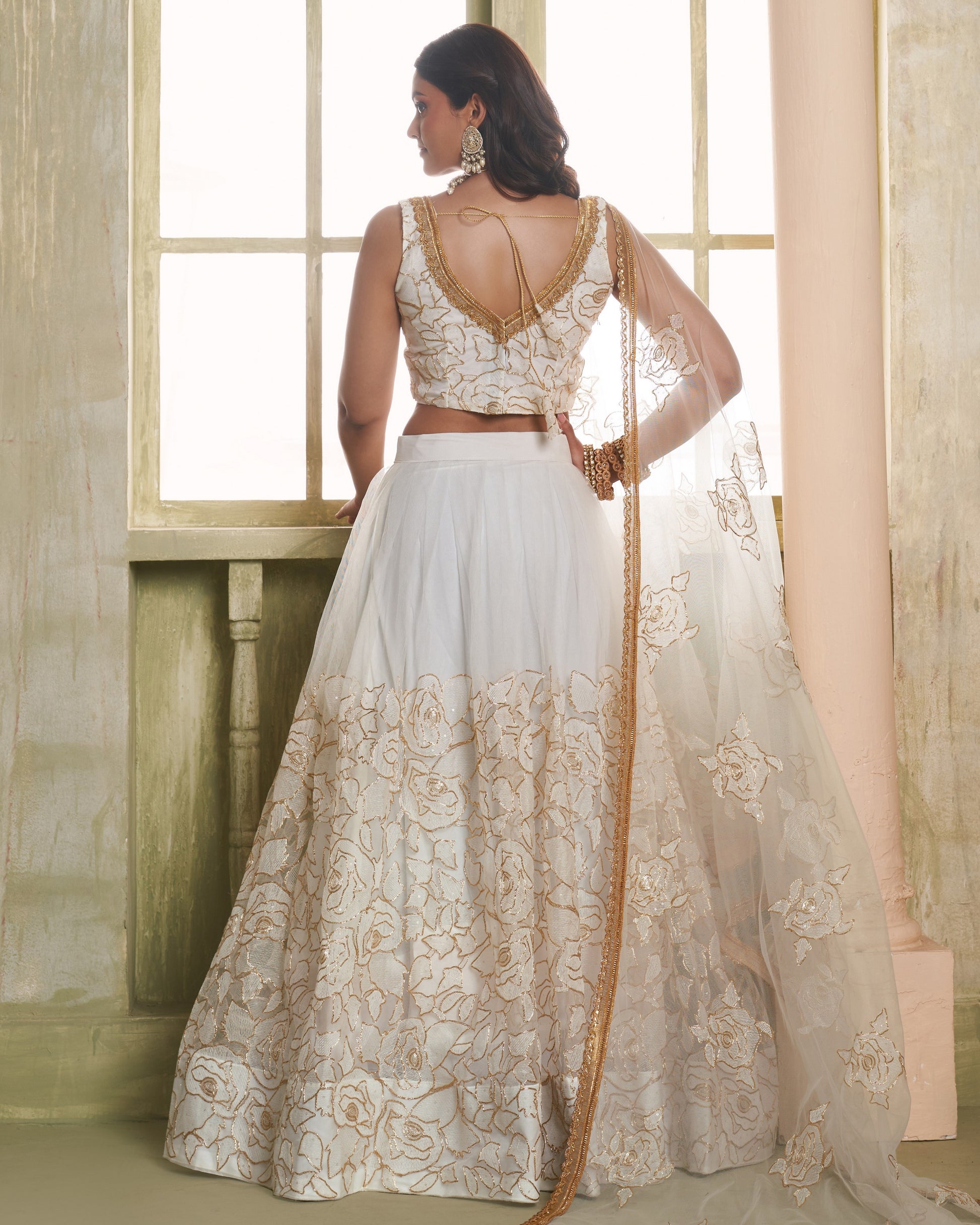 Woman wearing a white and gold traditional outfit with a flowing skirt in a softly lit room.