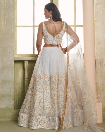 Woman wearing a white and gold traditional outfit with a flowing skirt in a softly lit room.