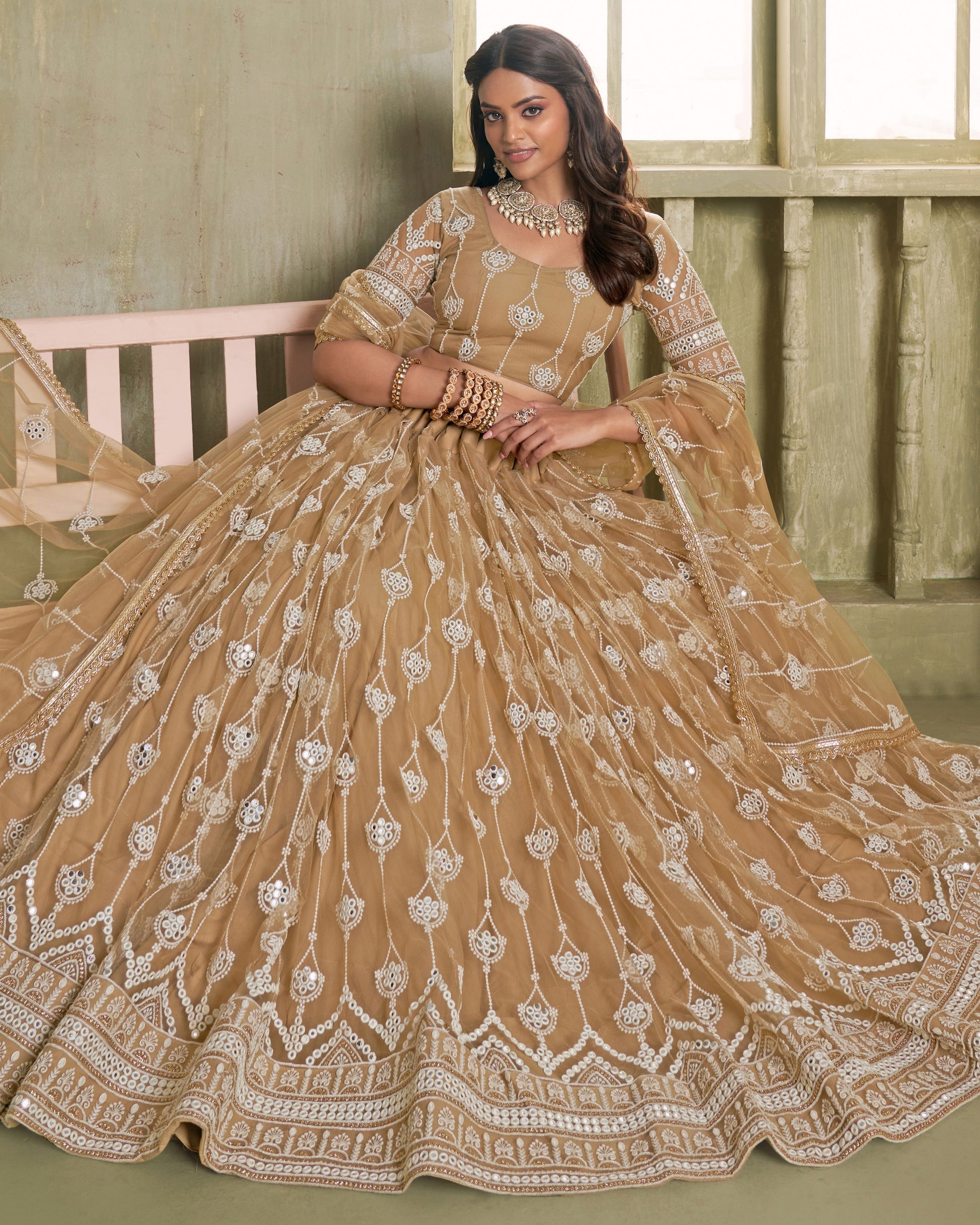 Woman in a beige embroidered traditional outfit sitting on a bench.