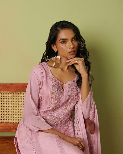 Woman in a pink traditional outfit sitting on a chair against a green wall