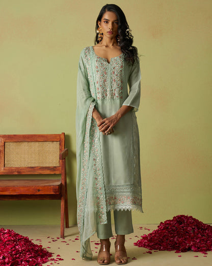Woman in a light green traditional outfit with floral patterns on a yellow background