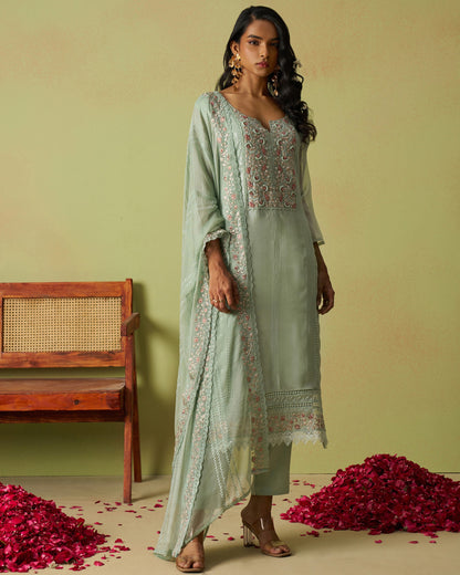 Woman in a light green traditional outfit with floral patterns standing against a plain background