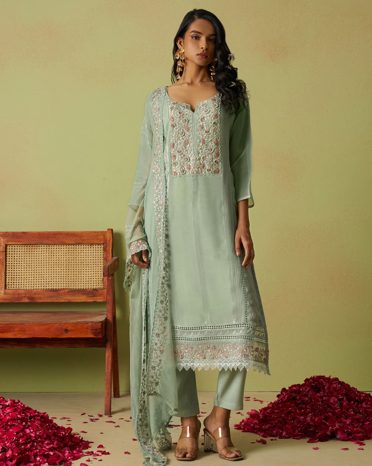 Woman wearing a light green traditional outfit with floral patterns against a green background.